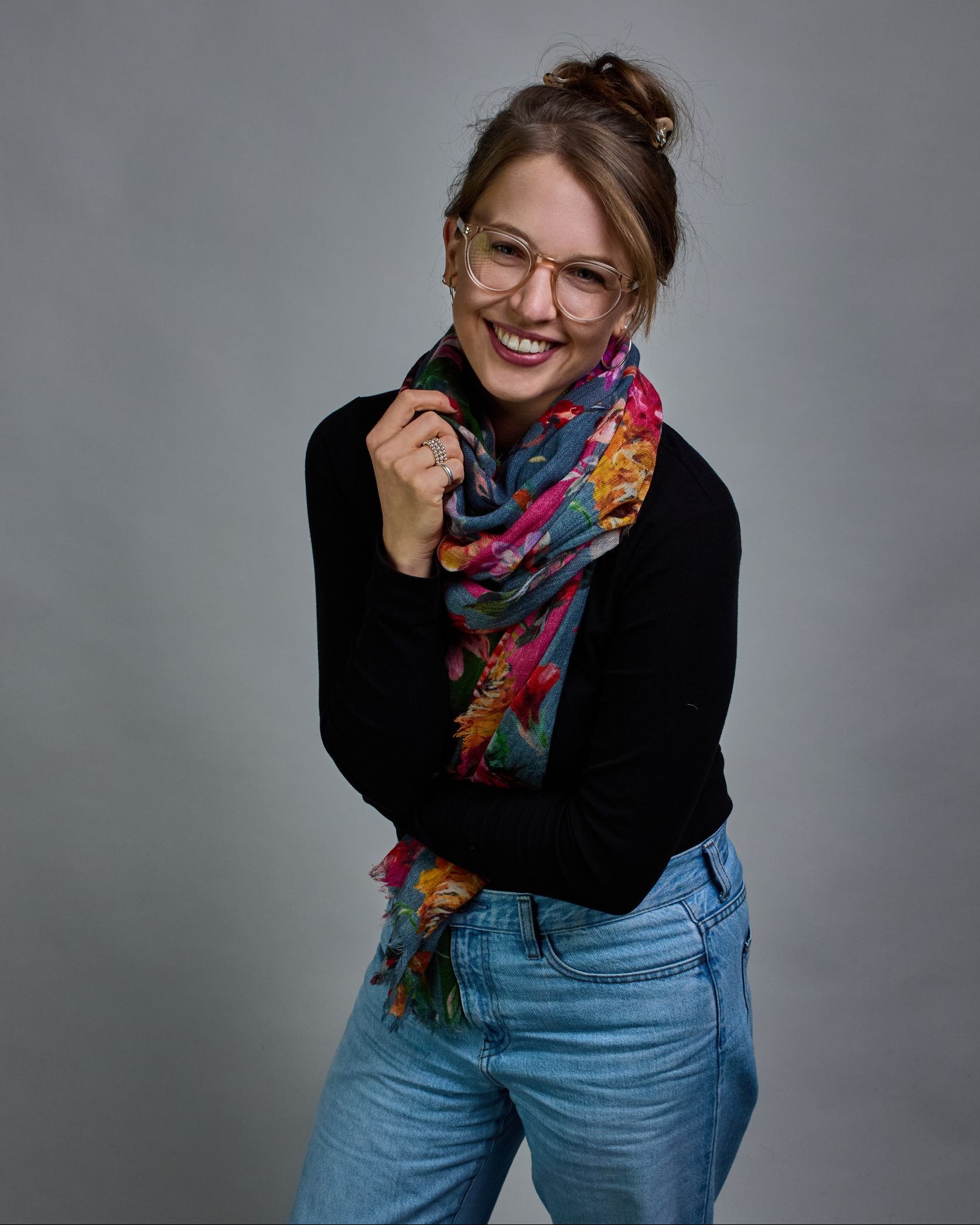 Ein Schal aus 75 % Wolle und 25 % Modal mit den Maßen 70 × 180 cm. Je nach Bild ist er locker um den Nacken gelegt oder einmal gewickelt, um eine lockere Schlaufe um den Hals zu haben, oder zweimal gewickelt, um das Maximum an Wärme zu bekommen. An den Kanten ist er leicht gefranst. Die Hintergrundfarbe des Schals ist blau, und er hat an einer Kante einen magentafarbenen und an der gegenüberliegenden Kante einen grünen Streifen. Auf dem ganzen Schal sind Blumen in Rot-, Orange-, Weiß- und Pinktönen sowie B…