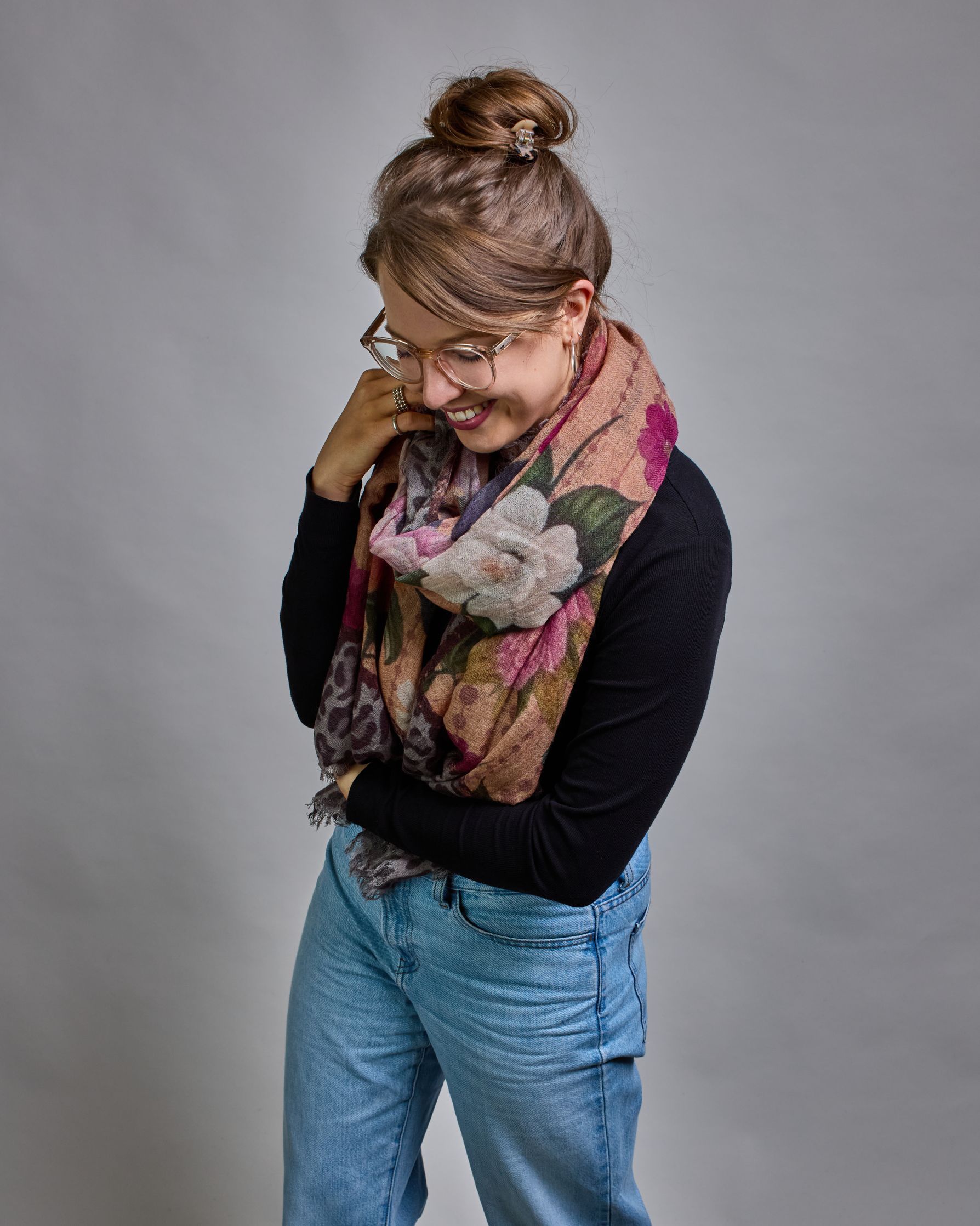 Ein Schal aus 75 % Wolle und 25 % Modal mit den Maßen 70 × 180 cm. Je nach Bild ist er locker um den Nacken gelegt oder einmal gewickelt, um eine lockere Schlaufe um den Hals zu haben, oder zweimal gewickelt, um das Maximum an Wärme zu bekommen. An den Kanten ist er leicht gefranst. Die Hintergrundfarbe des Schals ist ein rosastichiges Beige und an den Kanten ist ein Rahmen in einem Leomuster in verschiedenen Grautönen. Auf dem ganzen Schal sind verschiedene Blüten in unterschiedlichen Rosa-, und Weißtönen…