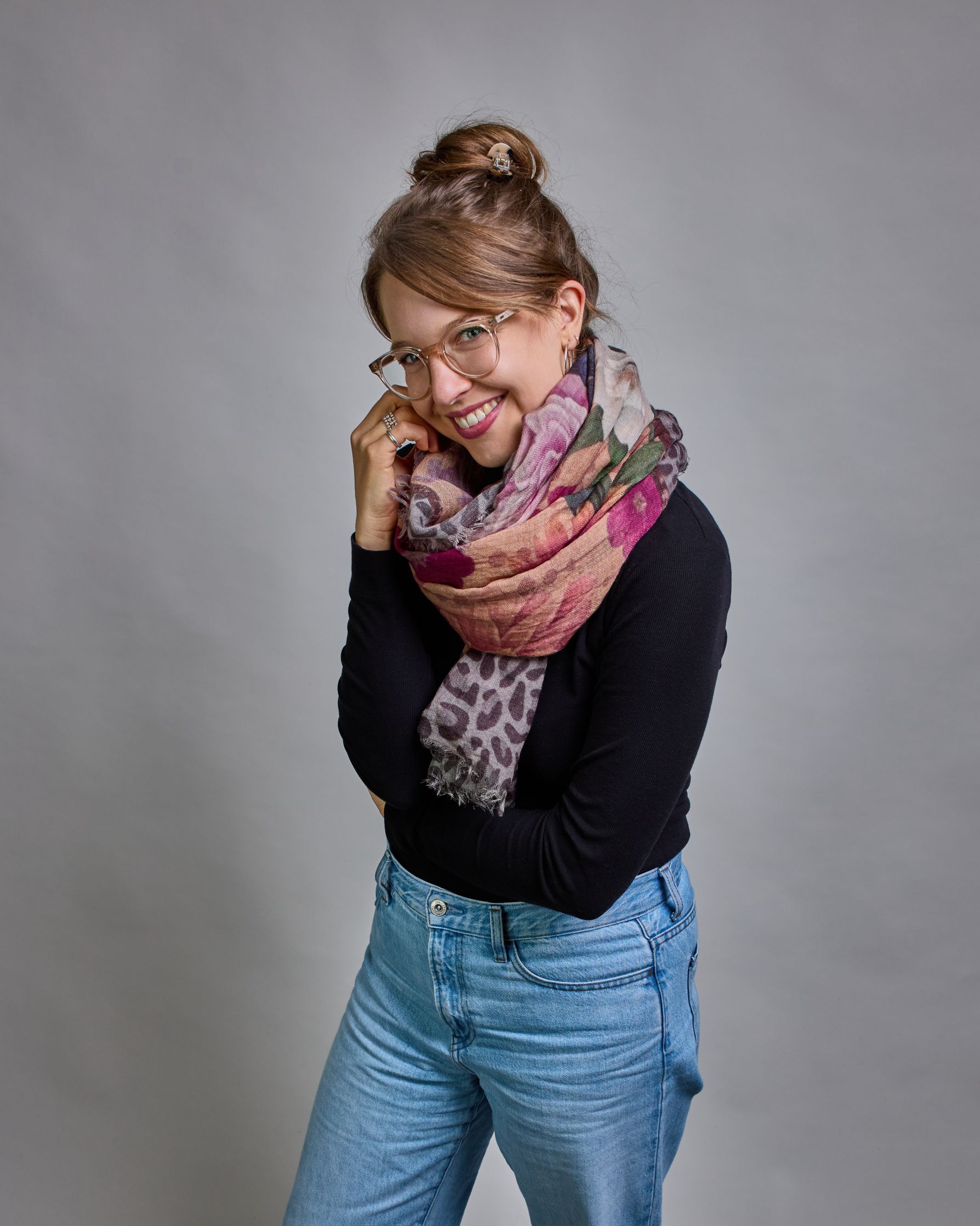 Ein Schal aus 75 % Wolle und 25 % Modal mit den Maßen 70 × 180 cm. Je nach Bild ist er locker um den Nacken gelegt oder einmal gewickelt, um eine lockere Schlaufe um den Hals zu haben, oder zweimal gewickelt, um das Maximum an Wärme zu bekommen. An den Kanten ist er leicht gefranst. Die Hintergrundfarbe des Schals ist ein rosastichiges Beige und an den Kanten ist ein Rahmen in einem Leomuster in verschiedenen Grautönen. Auf dem ganzen Schal sind verschiedene Blüten in unterschiedlichen Rosa-, und Weißtönen…