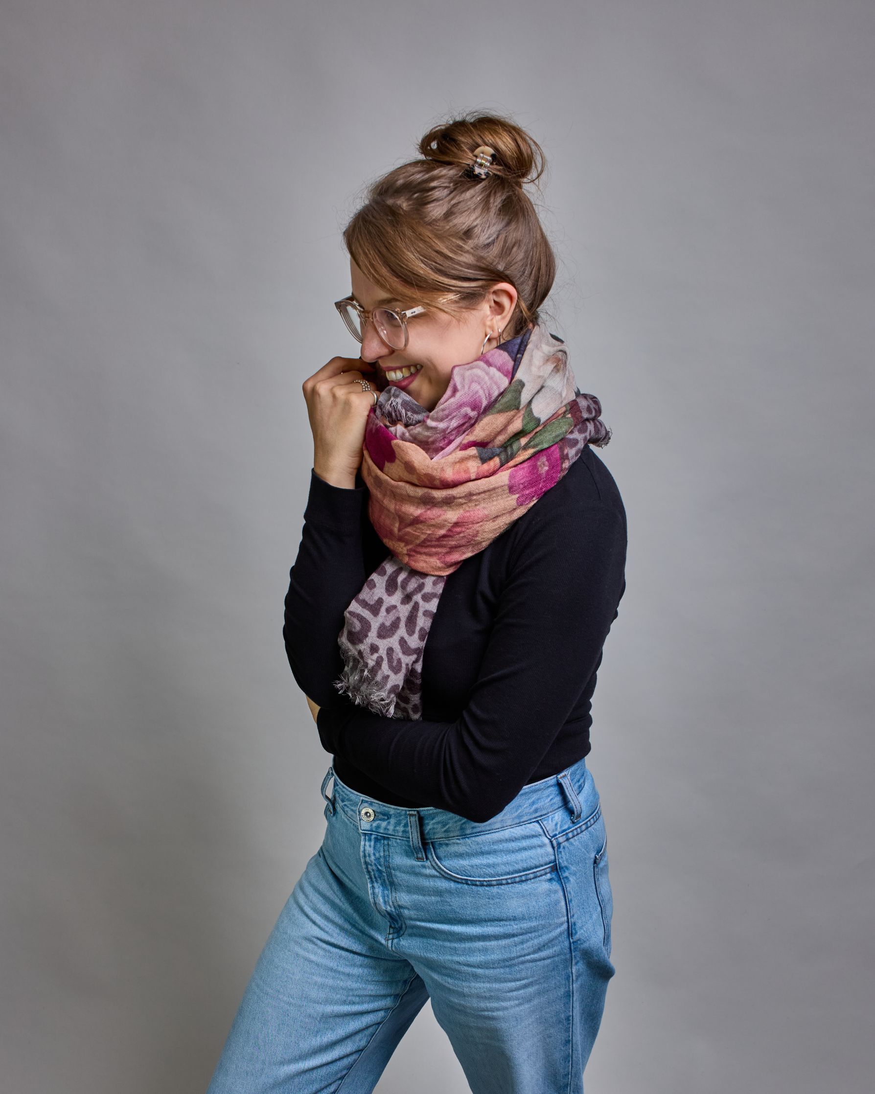 Ein Schal aus 75 % Wolle und 25 % Modal mit den Maßen 70 × 180 cm. Je nach Bild ist er locker um den Nacken gelegt oder einmal gewickelt, um eine lockere Schlaufe um den Hals zu haben, oder zweimal gewickelt, um das Maximum an Wärme zu bekommen. An den Kanten ist er leicht gefranst. Die Hintergrundfarbe des Schals ist ein rosastichiges Beige und an den Kanten ist ein Rahmen in einem Leomuster in verschiedenen Grautönen. Auf dem ganzen Schal sind verschiedene Blüten in unterschiedlichen Rosa-, und Weißtönen…