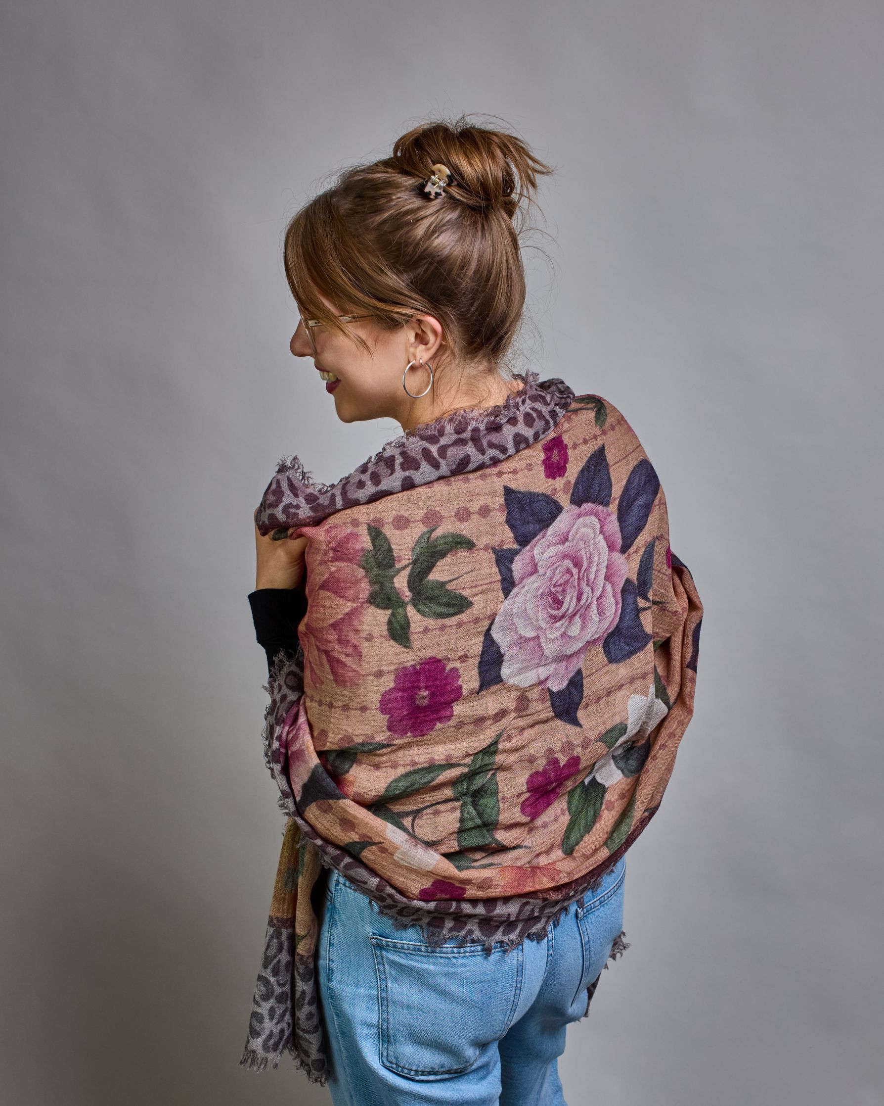 Ein Schal aus 75 % Wolle und 25 % Modal mit den Maßen 70 × 180 cm. Je nach Bild ist er locker um den Nacken gelegt oder einmal gewickelt, um eine lockere Schlaufe um den Hals zu haben, oder zweimal gewickelt, um das Maximum an Wärme zu bekommen. An den Kanten ist er leicht gefranst. Die Hintergrundfarbe des Schals ist ein rosastichiges Beige und an den Kanten ist ein Rahmen in einem Leomuster in verschiedenen Grautönen. Auf dem ganzen Schal sind verschiedene Blüten in unterschiedlichen Rosa-, und Weißtönen…