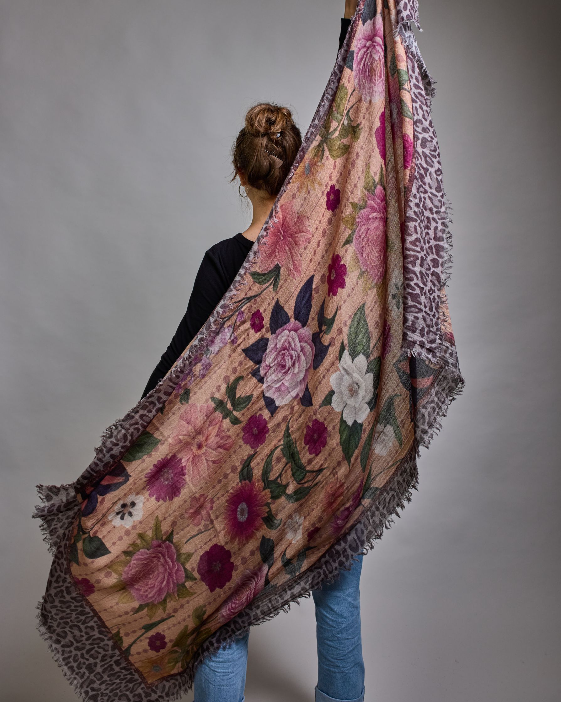 Ein Schal aus 75 % Wolle und 25 % Modal mit den Maßen 70 × 180 cm. Je nach Bild ist er locker um den Nacken gelegt oder einmal gewickelt, um eine lockere Schlaufe um den Hals zu haben, oder zweimal gewickelt, um das Maximum an Wärme zu bekommen. An den Kanten ist er leicht gefranst. Die Hintergrundfarbe des Schals ist ein rosastichiges Beige und an den Kanten ist ein Rahmen in einem Leomuster in verschiedenen Grautönen. Auf dem ganzen Schal sind verschiedene Blüten in unterschiedlichen Rosa-, und Weißtönen…