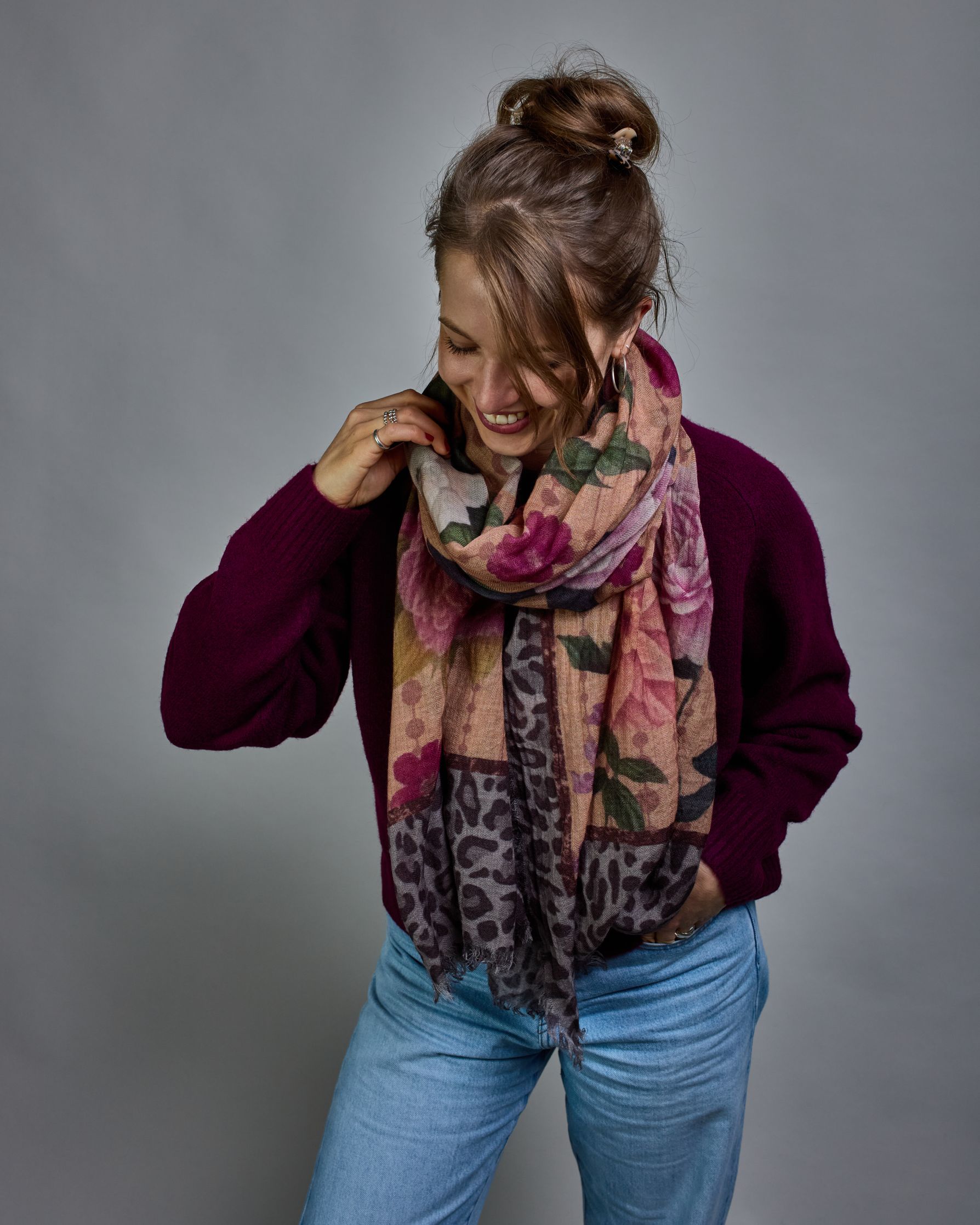 Ein Schal aus 75 % Wolle und 25 % Modal mit den Maßen 70 × 180 cm. Je nach Bild ist er locker um den Nacken gelegt oder einmal gewickelt, um eine lockere Schlaufe um den Hals zu haben, oder zweimal gewickelt, um das Maximum an Wärme zu bekommen. An den Kanten ist er leicht gefranst. Die Hintergrundfarbe des Schals ist ein rosastichiges Beige und an den Kanten ist ein Rahmen in einem Leomuster in verschiedenen Grautönen. Auf dem ganzen Schal sind verschiedene Blüten in unterschiedlichen Rosa-, und Weißtönen…