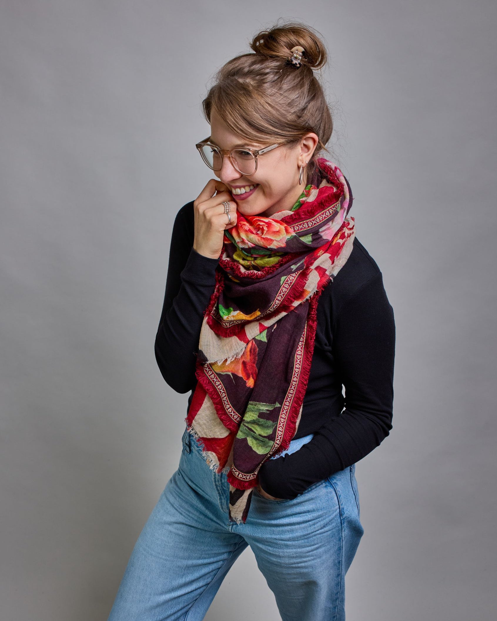 Ein Schal aus 75 % Wolle und 25 % Modal mit den Maßen 70 × 180 cm. Je nach Bild ist er locker um den Nacken gelegt oder einmal gewickelt, um eine lockere Schlaufe um den Hals zu haben, oder zweimal gewickelt, um das Maximum an Wärme zu bekommen. An den Kanten ist er leicht gefranst. Die Hintergrundfarbe des Schals ist schwarz, und er hat an den Kanten einen rot-weiß gemusterten Rahmen. Zwischen diesem Rahmen und dem restlichen Design des Schals ist in einem festen Stoff eine schmale symmetrisch gemusterte…