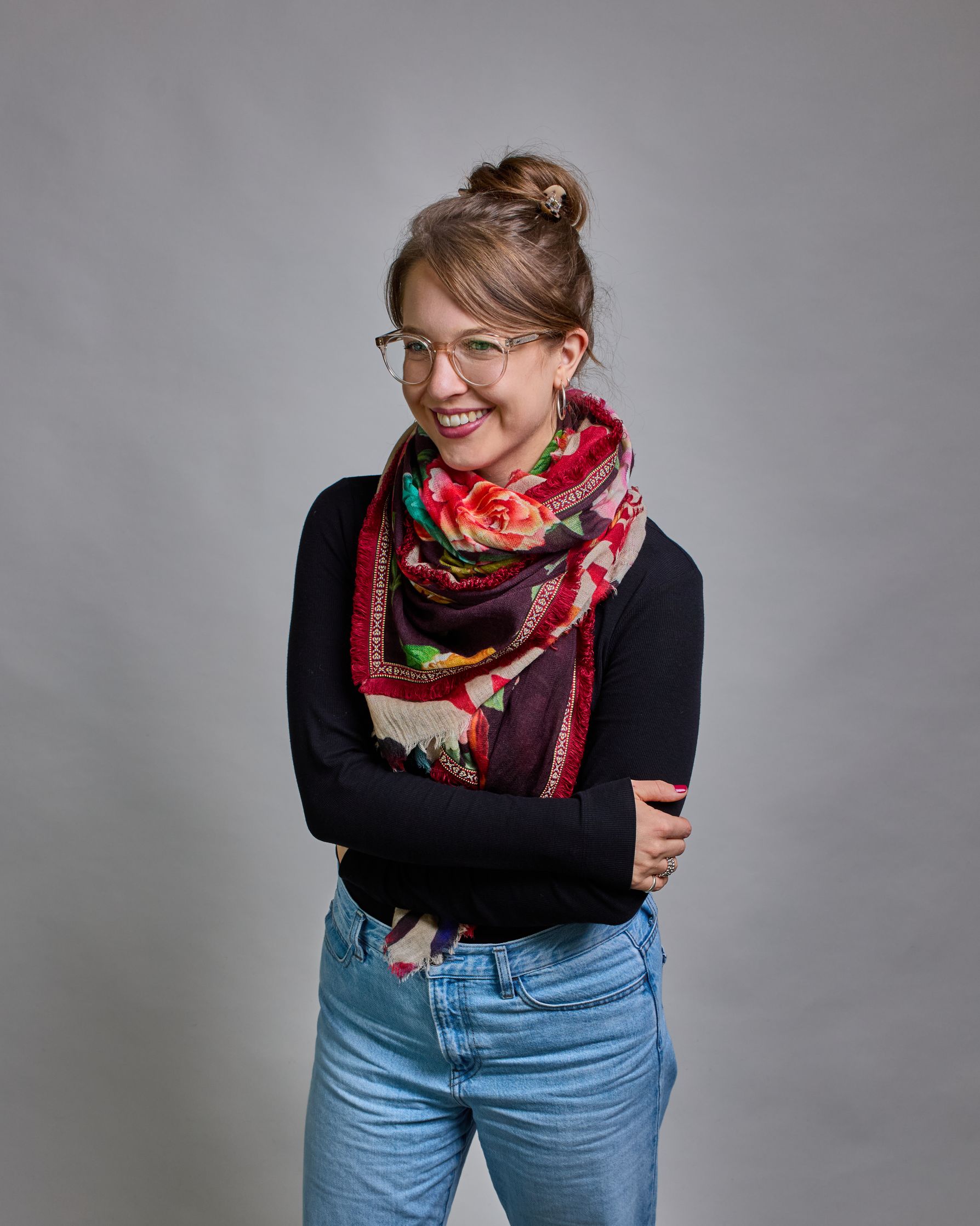 Ein Schal aus 75 % Wolle und 25 % Modal mit den Maßen 70 × 180 cm. Je nach Bild ist er locker um den Nacken gelegt oder einmal gewickelt, um eine lockere Schlaufe um den Hals zu haben, oder zweimal gewickelt, um das Maximum an Wärme zu bekommen. An den Kanten ist er leicht gefranst. Die Hintergrundfarbe des Schals ist schwarz, und er hat an den Kanten einen rot-weiß gemusterten Rahmen. Zwischen diesem Rahmen und dem restlichen Design des Schals ist in einem festen Stoff eine schmale symmetrisch gemusterte…