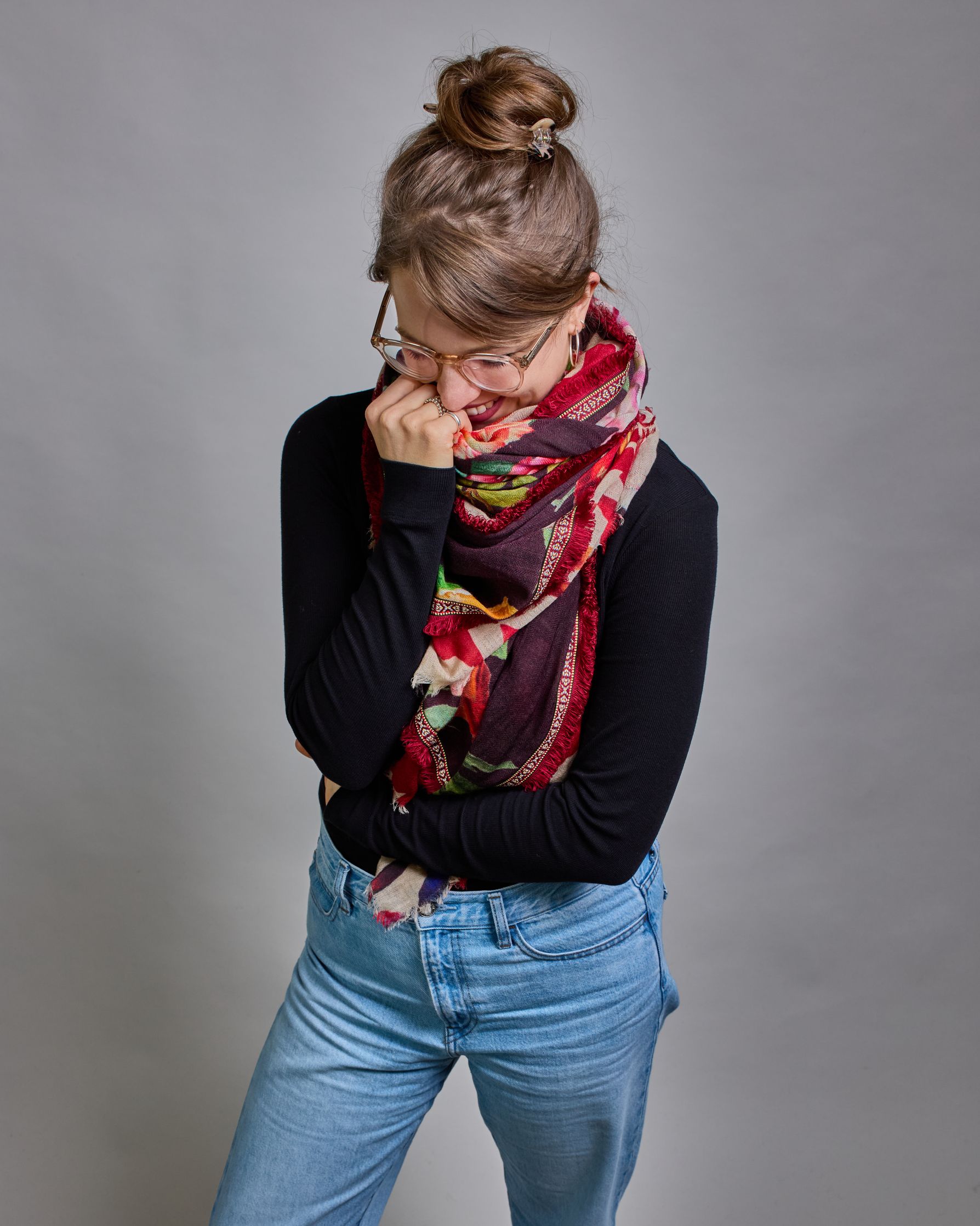 Ein Schal aus 75 % Wolle und 25 % Modal mit den Maßen 70 × 180 cm. Je nach Bild ist er locker um den Nacken gelegt oder einmal gewickelt, um eine lockere Schlaufe um den Hals zu haben, oder zweimal gewickelt, um das Maximum an Wärme zu bekommen. An den Kanten ist er leicht gefranst. Die Hintergrundfarbe des Schals ist schwarz, und er hat an den Kanten einen rot-weiß gemusterten Rahmen. Zwischen diesem Rahmen und dem restlichen Design des Schals ist in einem festen Stoff eine schmale symmetrisch gemusterte…