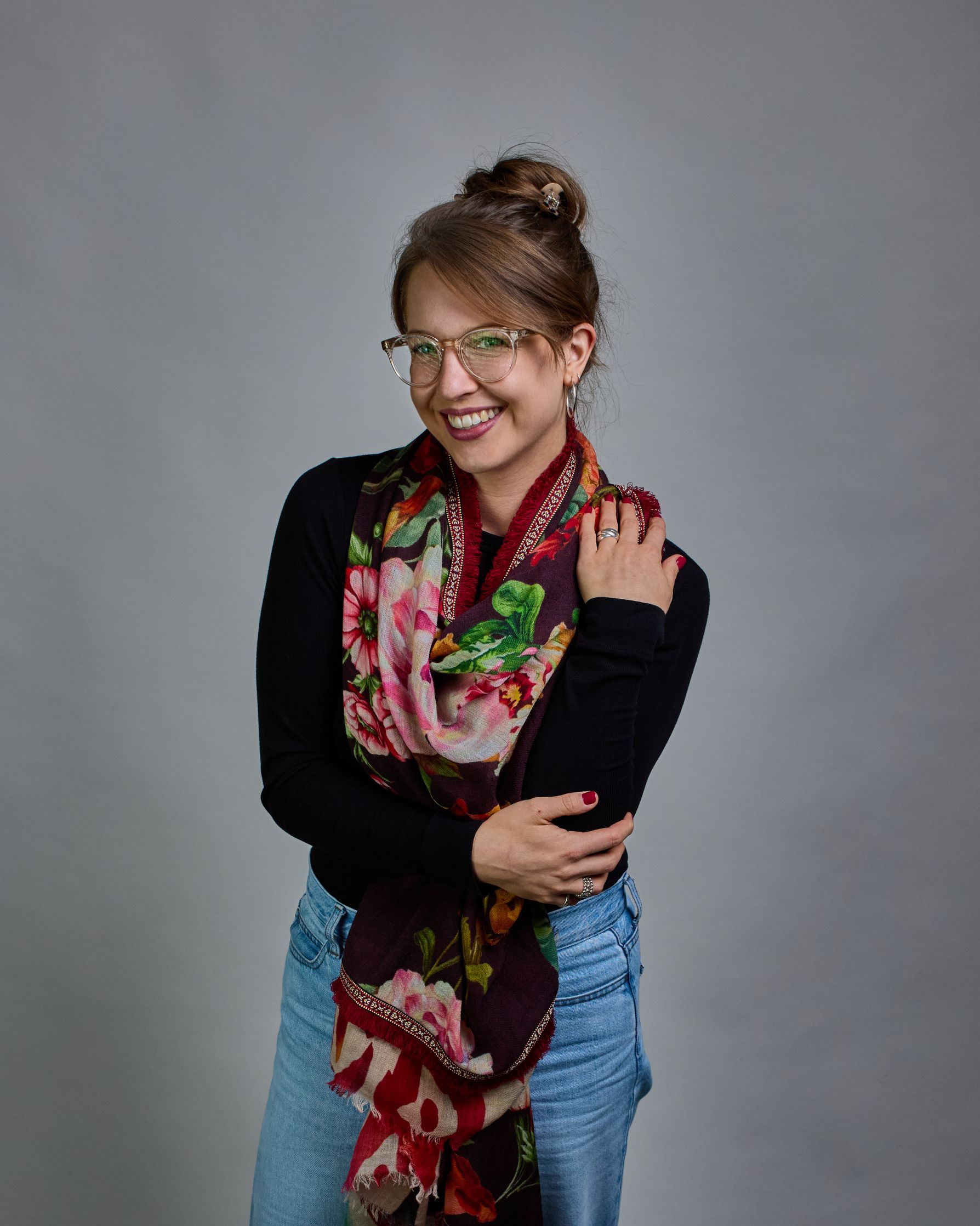 Ein Schal aus 75 % Wolle und 25 % Modal mit den Maßen 70 × 180 cm. Je nach Bild ist er locker um den Nacken gelegt oder einmal gewickelt, um eine lockere Schlaufe um den Hals zu haben, oder zweimal gewickelt, um das Maximum an Wärme zu bekommen. An den Kanten ist er leicht gefranst. Die Hintergrundfarbe des Schals ist schwarz, und er hat an den Kanten einen rot-weiß gemusterten Rahmen. Zwischen diesem Rahmen und dem restlichen Design des Schals ist in einem festen Stoff eine schmale symmetrisch gemusterte…