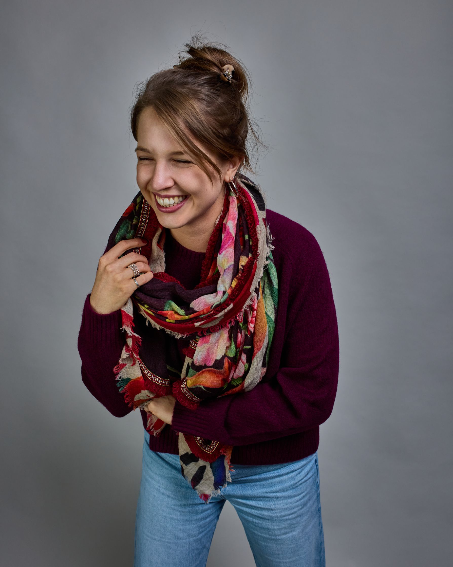 Ein Schal aus 75 % Wolle und 25 % Modal mit den Maßen 70 × 180 cm. Je nach Bild ist er locker um den Nacken gelegt oder einmal gewickelt, um eine lockere Schlaufe um den Hals zu haben, oder zweimal gewickelt, um das Maximum an Wärme zu bekommen. An den Kanten ist er leicht gefranst. Die Hintergrundfarbe des Schals ist schwarz, und er hat an den Kanten einen rot-weiß gemusterten Rahmen. Zwischen diesem Rahmen und dem restlichen Design des Schals ist in einem festen Stoff eine schmale symmetrisch gemusterte…