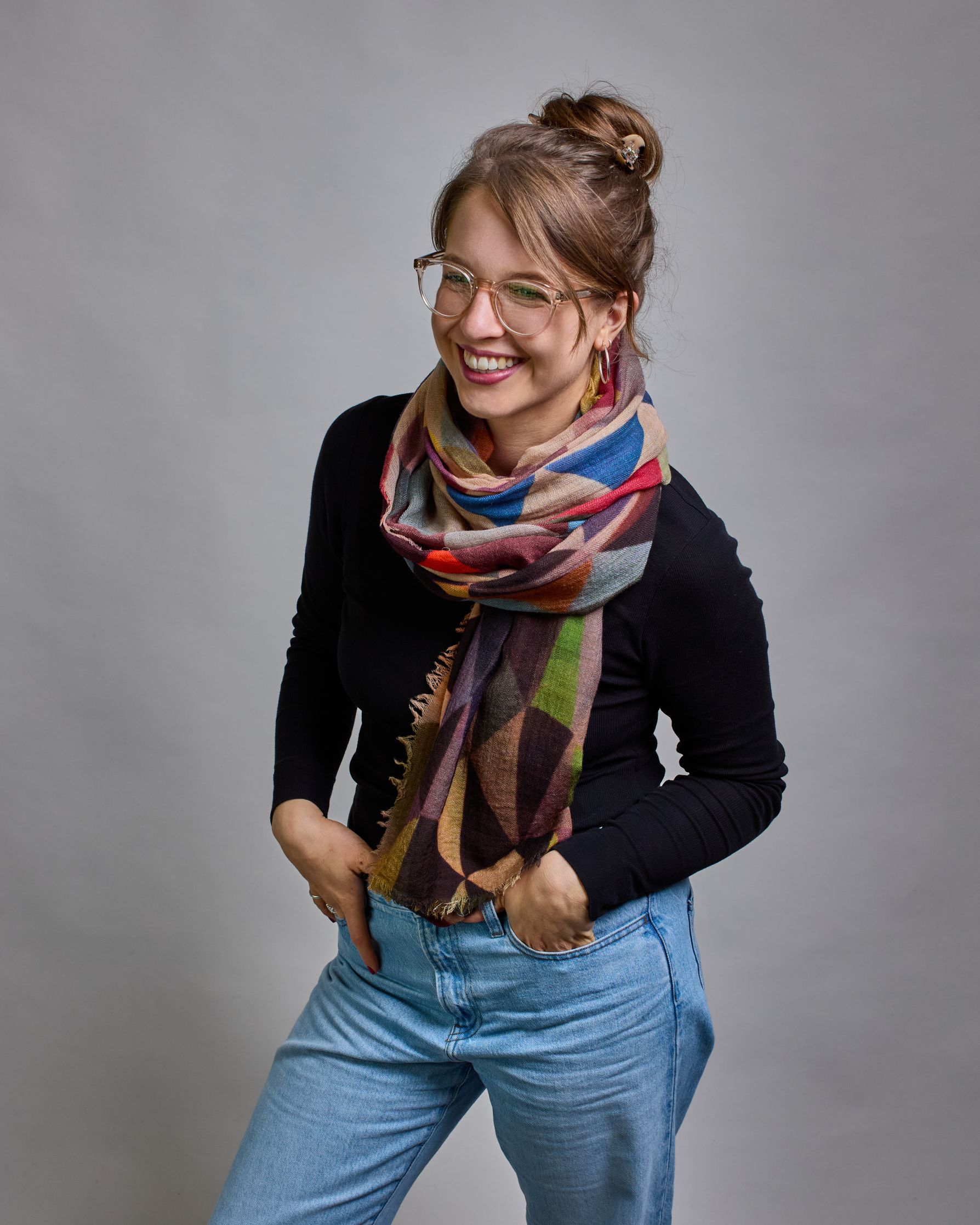 Ein Schal aus 75 % Wolle und 25 % Modal mit den Maßen 100 × 180 cm. Je nach Bild ist er locker um den Nacken gelegt oder einmal gewickelt, um eine lockere Schlaufe um den Hals zu haben, oder zweimal gewickelt, um das Maximum an Wärme zu bekommen. An den Kanten ist er leicht gefranst. Über den ganzen Schal ist ein symetrisches Dreieckmuster verteilt. Die Dreiecke sind in Grau-, Rot-, Blau- Rosa-, Lila-, Grün- und Brauntönen gehalten. #1