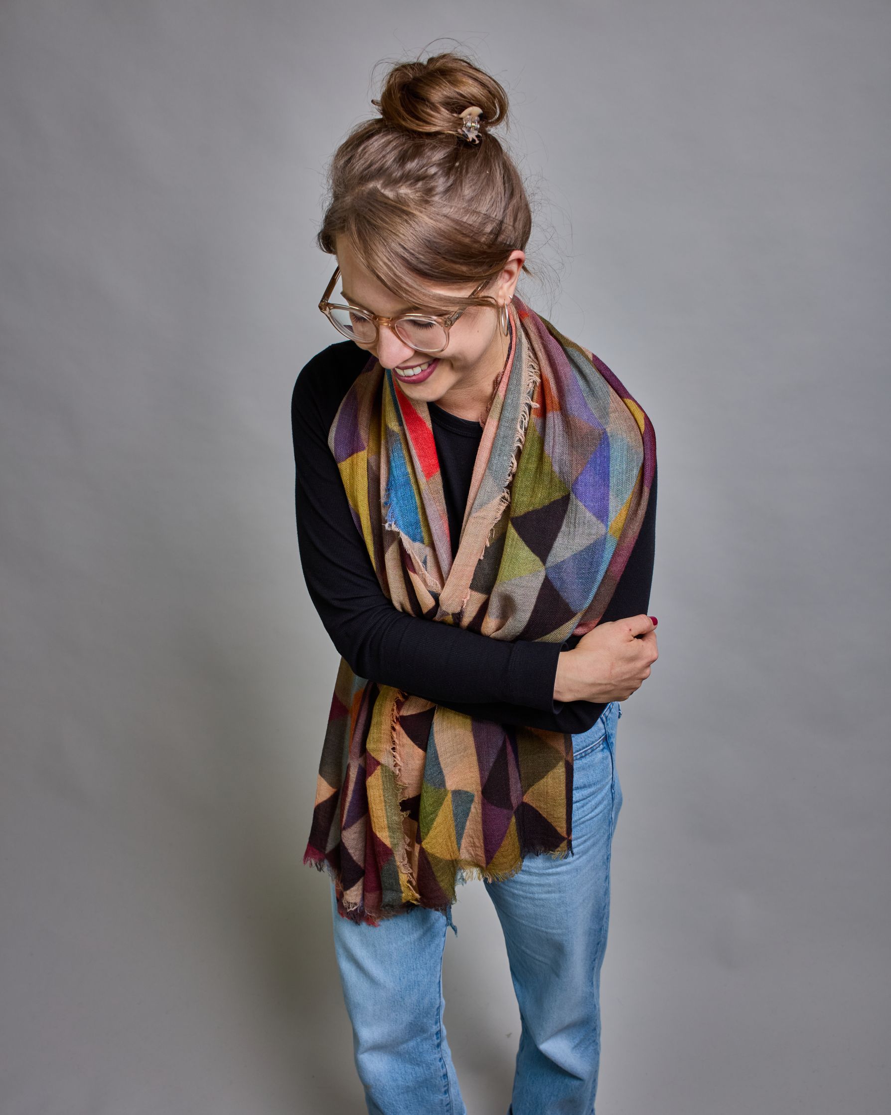 Ein Schal aus 75 % Wolle und 25 % Modal mit den Maßen 100 × 180 cm. Je nach Bild ist er locker um den Nacken gelegt oder einmal gewickelt, um eine lockere Schlaufe um den Hals zu haben, oder zweimal gewickelt, um das Maximum an Wärme zu bekommen. An den Kanten ist er leicht gefranst. Über den ganzen Schal ist ein symetrisches Dreieckmuster verteilt. Die Dreiecke sind in Grau-, Rot-, Blau- Rosa-, Lila-, Grün- und Brauntönen gehalten. #3