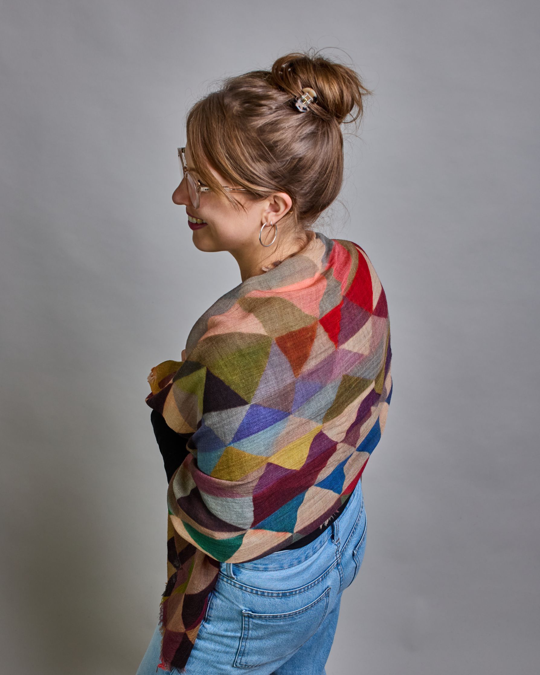 Ein Schal aus 75 % Wolle und 25 % Modal mit den Maßen 100 × 180 cm. Je nach Bild ist er locker um den Nacken gelegt oder einmal gewickelt, um eine lockere Schlaufe um den Hals zu haben, oder zweimal gewickelt, um das Maximum an Wärme zu bekommen. An den Kanten ist er leicht gefranst. Über den ganzen Schal ist ein symetrisches Dreieckmuster verteilt. Die Dreiecke sind in Grau-, Rot-, Blau- Rosa-, Lila-, Grün- und Brauntönen gehalten. #4