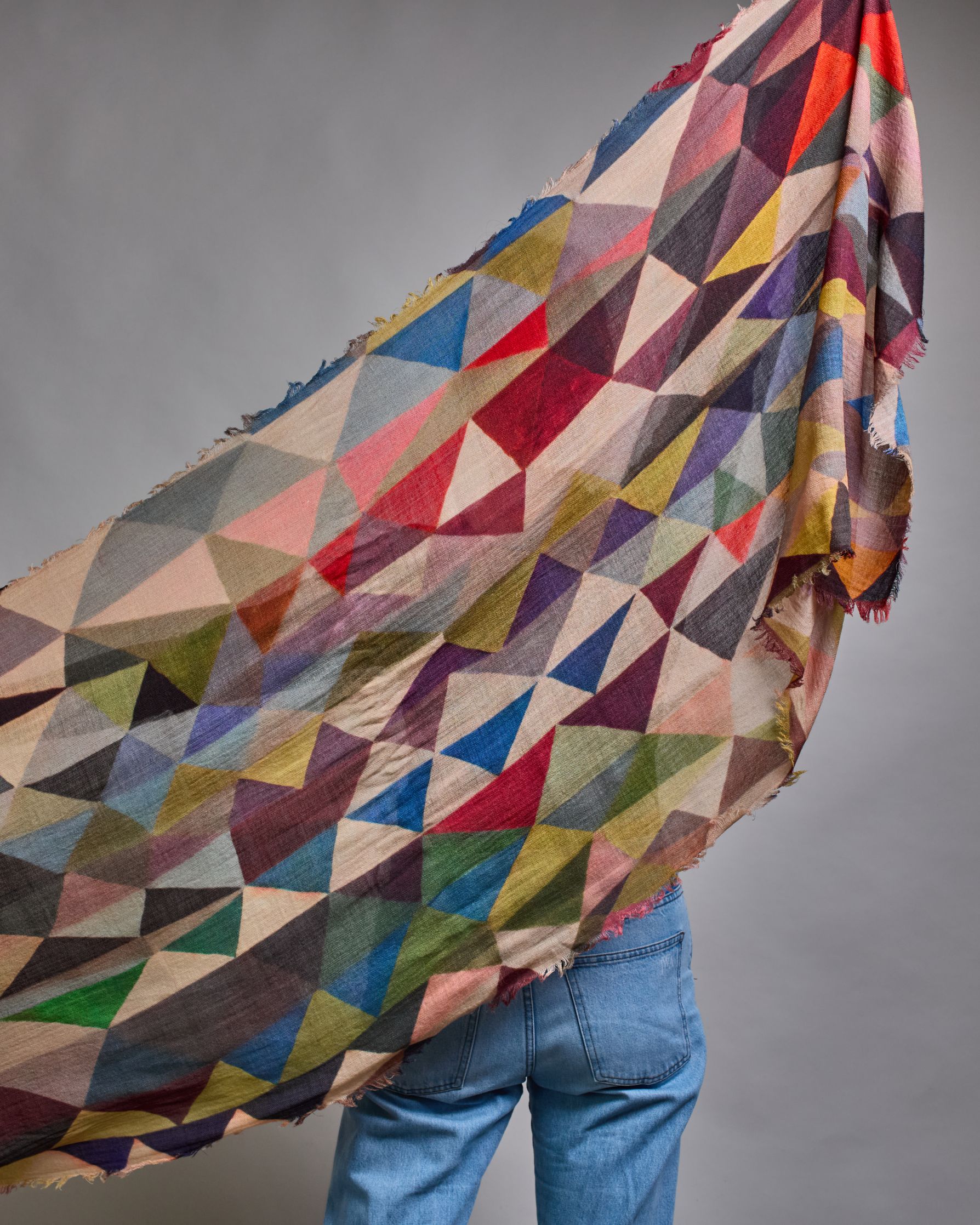 Ein Schal aus 75 % Wolle und 25 % Modal mit den Maßen 100 × 180 cm. Je nach Bild ist er locker um den Nacken gelegt oder einmal gewickelt, um eine lockere Schlaufe um den Hals zu haben, oder zweimal gewickelt, um das Maximum an Wärme zu bekommen. An den Kanten ist er leicht gefranst. Über den ganzen Schal ist ein symetrisches Dreieckmuster verteilt. Die Dreiecke sind in Grau-, Rot-, Blau- Rosa-, Lila-, Grün- und Brauntönen gehalten. #5