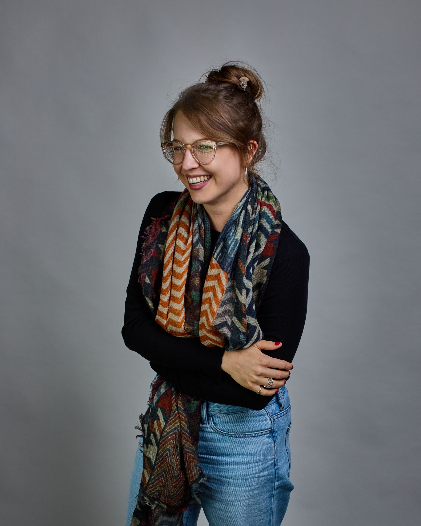 Ein Schal aus 75 % Wolle und 25 % Modal mit den Maßen 100 × 180 cm. Je nach Bild ist er locker um den Nacken gelegt oder einmal gewickelt, um eine lockere Schlaufe um den Hals zu haben, oder zweimal gewickelt, um das Maximum an Wärme zu bekommen. An den Kanten ist er leicht gefranst. Der Schal ist in einem Patchworkstil designt, in welchem jedes Rechteck Zickzackmuster in unterschiedlichen Größen und Farben hat. Die primären Farben sind verschiedene Grautöne, Orange, Rot, Grün, Blautöne, Türkis und Beige.…