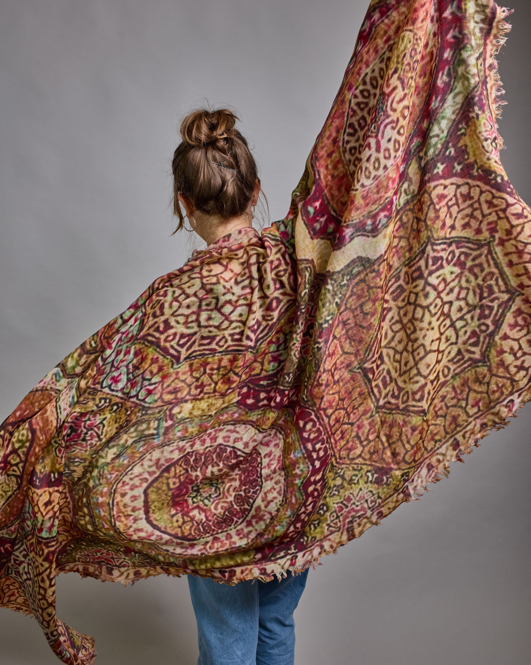 Ein Schal aus 75 % Wolle und 25 % Modal mit den Maßen 100 × 180 cm. Je nach Bild ist er locker um den Nacken gelegt oder einmal gewickelt, um eine lockere Schlaufe um den Hals zu haben, oder zweimal gewickelt, um das Maximum an Wärme zu bekommen. An den Kanten ist er leicht gefranst. Das Muster des Schals ist orientalisch inspiriert und besteht aus unterschiedlichen Ornamenten in verschiedenen Beige- beziehungsweise Gelb- oder Brauntönen und Akzenten aus Pink- Grün-, und Türkistönen. #6