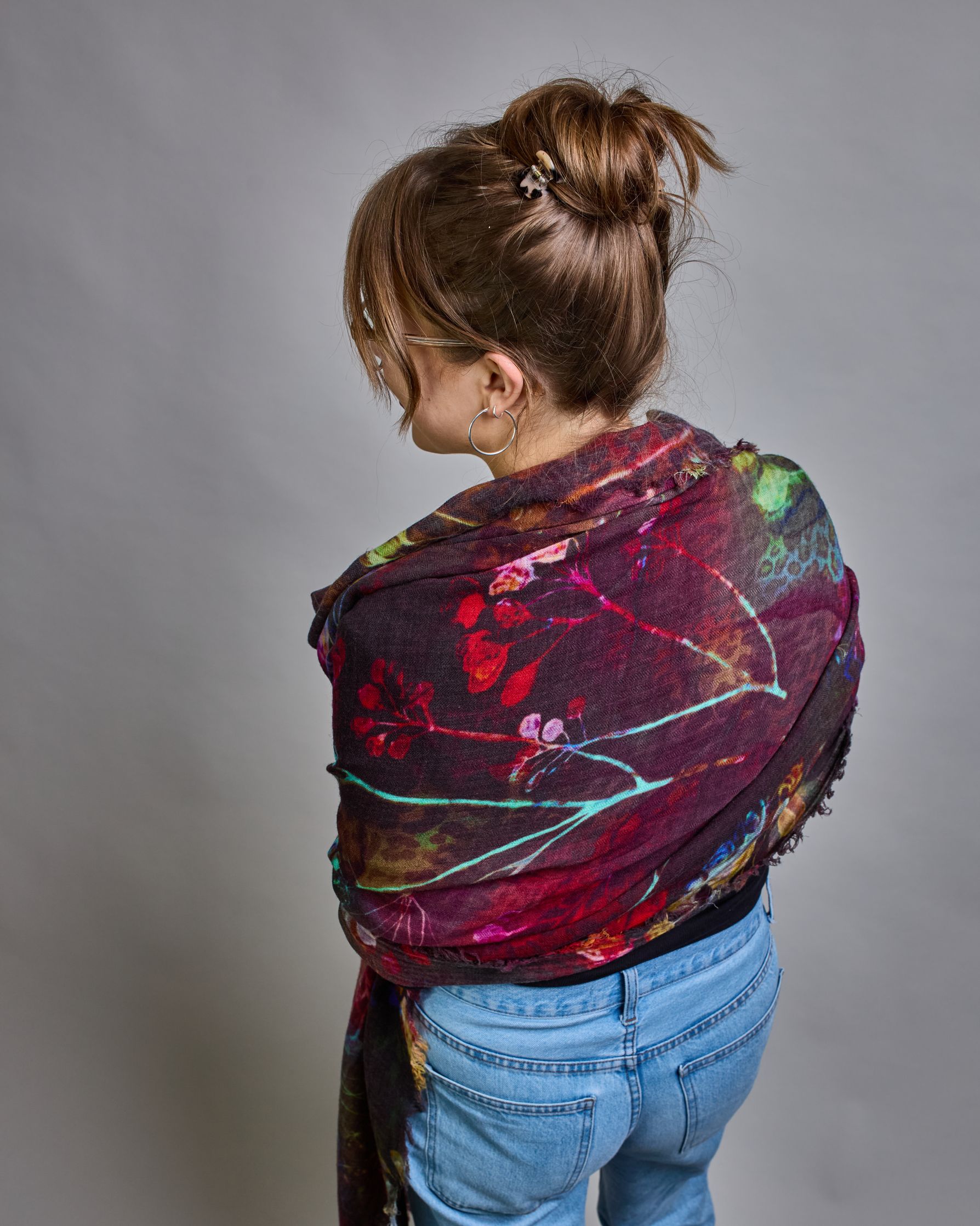 Ein Schal aus 75 % Wolle und 25 % Modal mit den Maßen 100 × 180 cm. Je nach Bild ist er locker um den Nacken gelegt oder einmal gewickelt, um eine lockere Schlaufe um den Hals zu haben, oder zweimal gewickelt, um das Maximum an Wärme zu bekommen. An den Kanten ist er leicht gefranst. Die Hintergrundfarbe des Schals ist Schwarz während sich filigrane Pusteblumen und Blätter in leuchtenden Türkis-, Rot-, Gelb- und Rosatönen verteilen. #5