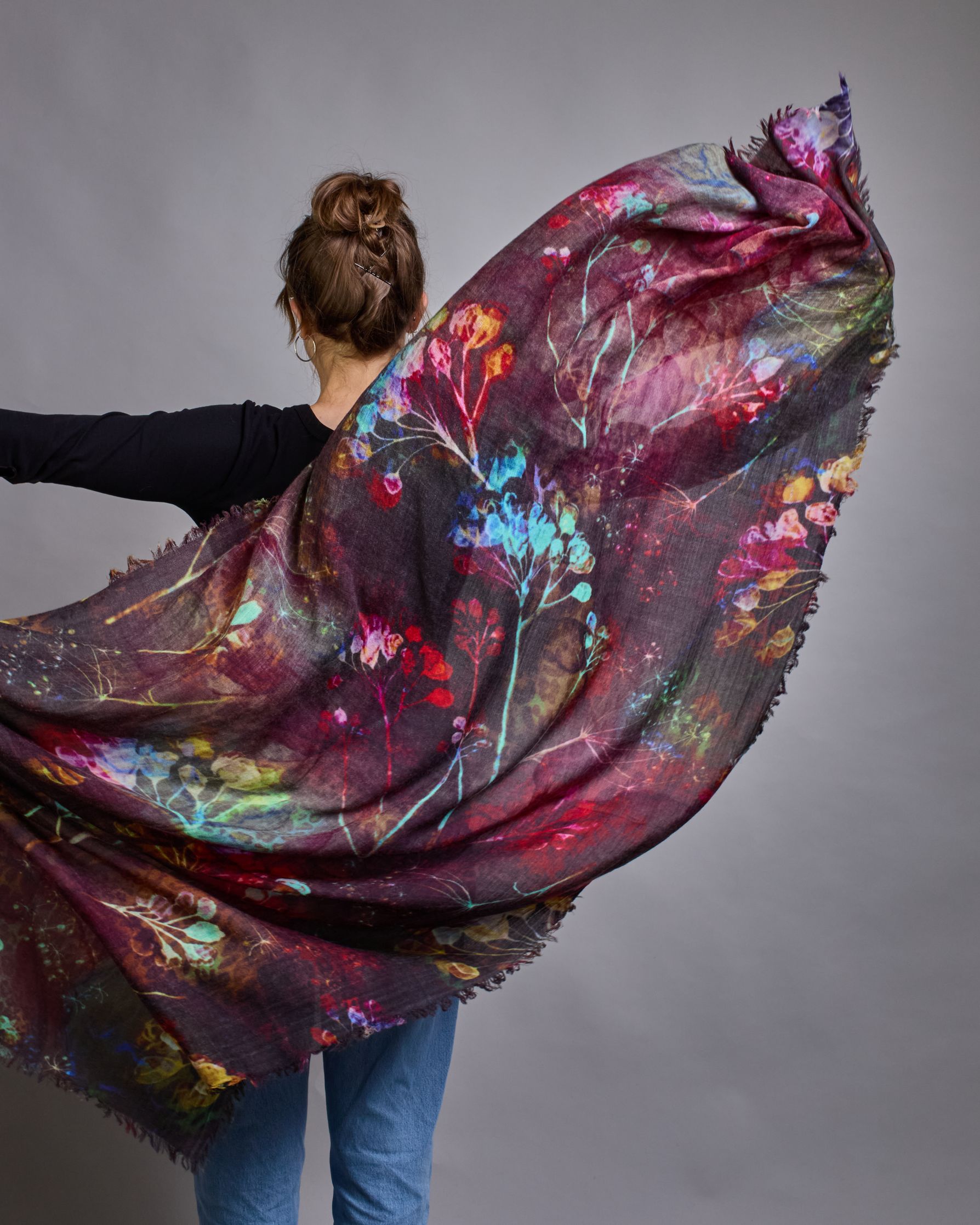 Ein Schal aus 75 % Wolle und 25 % Modal mit den Maßen 100 × 180 cm. Je nach Bild ist er locker um den Nacken gelegt oder einmal gewickelt, um eine lockere Schlaufe um den Hals zu haben, oder zweimal gewickelt, um das Maximum an Wärme zu bekommen. An den Kanten ist er leicht gefranst. Die Hintergrundfarbe des Schals ist Schwarz während sich filigrane Pusteblumen und Blätter in leuchtenden Türkis-, Rot-, Gelb- und Rosatönen verteilen. #6