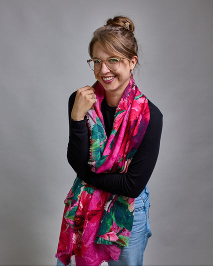 Ein Schal aus 75 % Wolle und 25 % Modal mit den Maßen 70 × 180 cm. Je nach Bild ist er locker um den Nacken gelegt oder einmal gewickelt, um eine lockere Schlaufe um den Hals zu haben, oder zweimal gewickelt, um das Maximum an Wärme zu bekommen. An den Kanten ist er leicht gefranst. Die Hintergrundfarbe des Schals ist pink. Auf dem ganzen Schal sind Blumen in Rot-, und Pinktönen sowie Blätter beziehungsweise Blumenstängel in verschiedenen Grüntönen verteilt. #4