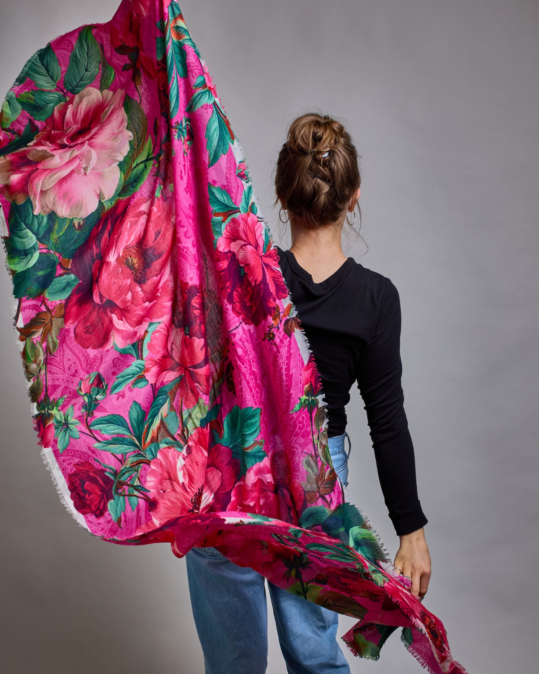 Ein Schal aus 75 % Wolle und 25 % Modal mit den Maßen 70 × 180 cm. Je nach Bild ist er locker um den Nacken gelegt oder einmal gewickelt, um eine lockere Schlaufe um den Hals zu haben, oder zweimal gewickelt, um das Maximum an Wärme zu bekommen. An den Kanten ist er leicht gefranst. Die Hintergrundfarbe des Schals ist pink. Auf dem ganzen Schal sind Blumen in Rot-, und Pinktönen sowie Blätter beziehungsweise Blumenstängel in verschiedenen Grüntönen verteilt. #6