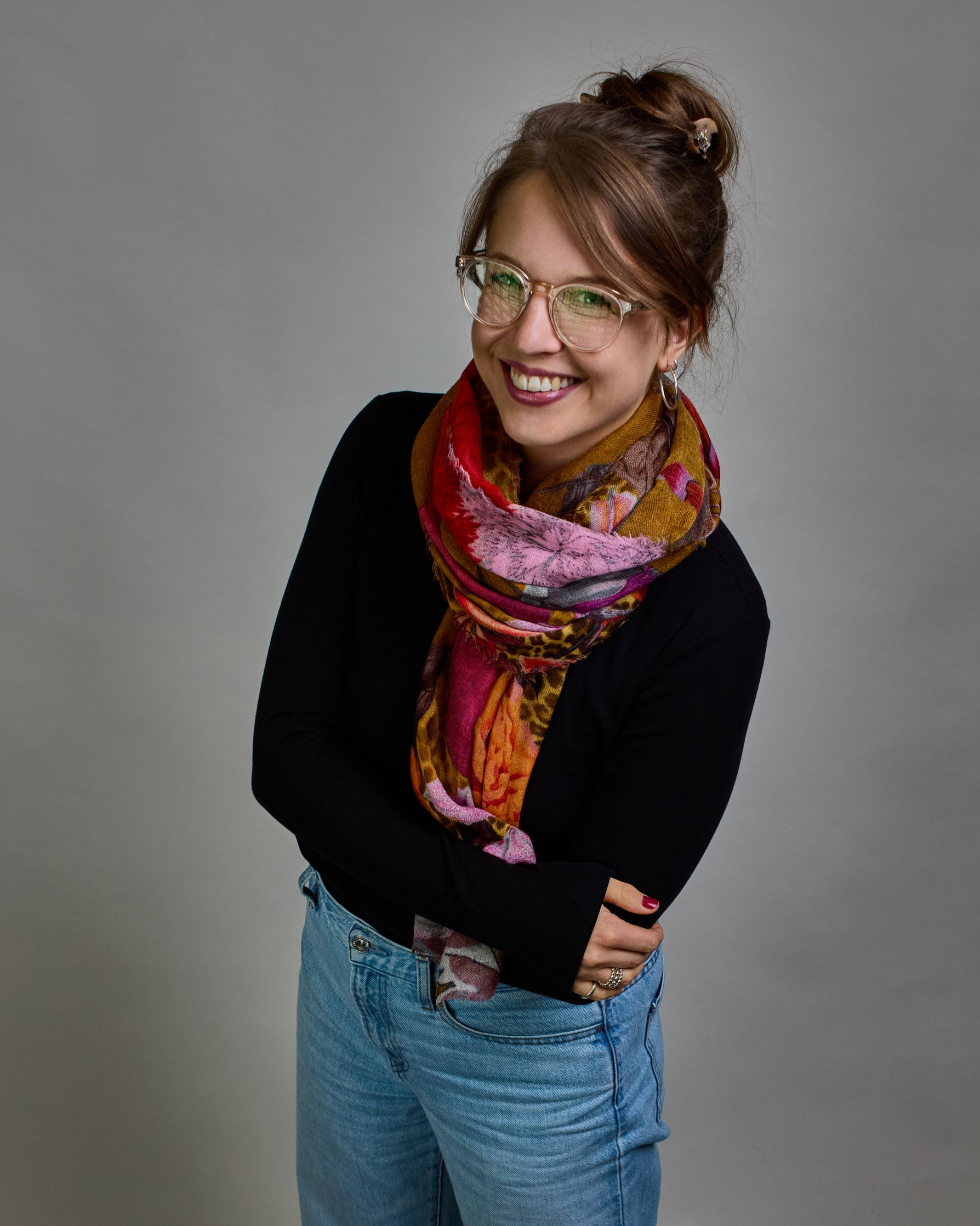 Ein Schal aus 75 % Wolle und 25 % Modal mit den Maßen 70 × 180 cm. Je nach Bild ist er locker um den Nacken gelegt oder einmal gewickelt, um eine lockere Schlaufe um den Hals zu haben, oder zweimal gewickelt, um das Maximum an Wärme zu bekommen. An den Kanten ist er leicht gefranst. Die Hintergrundfarbe des Schals ist Okker und hier und da ist ein Leomuster in Brauntönen zu sehen. Auf dem ganzen Schal sind Blumen in Rot-, Orange-, Weiß- und Pinktönen sowie Blätter beziehungsweise Blumenstängel in verschied…