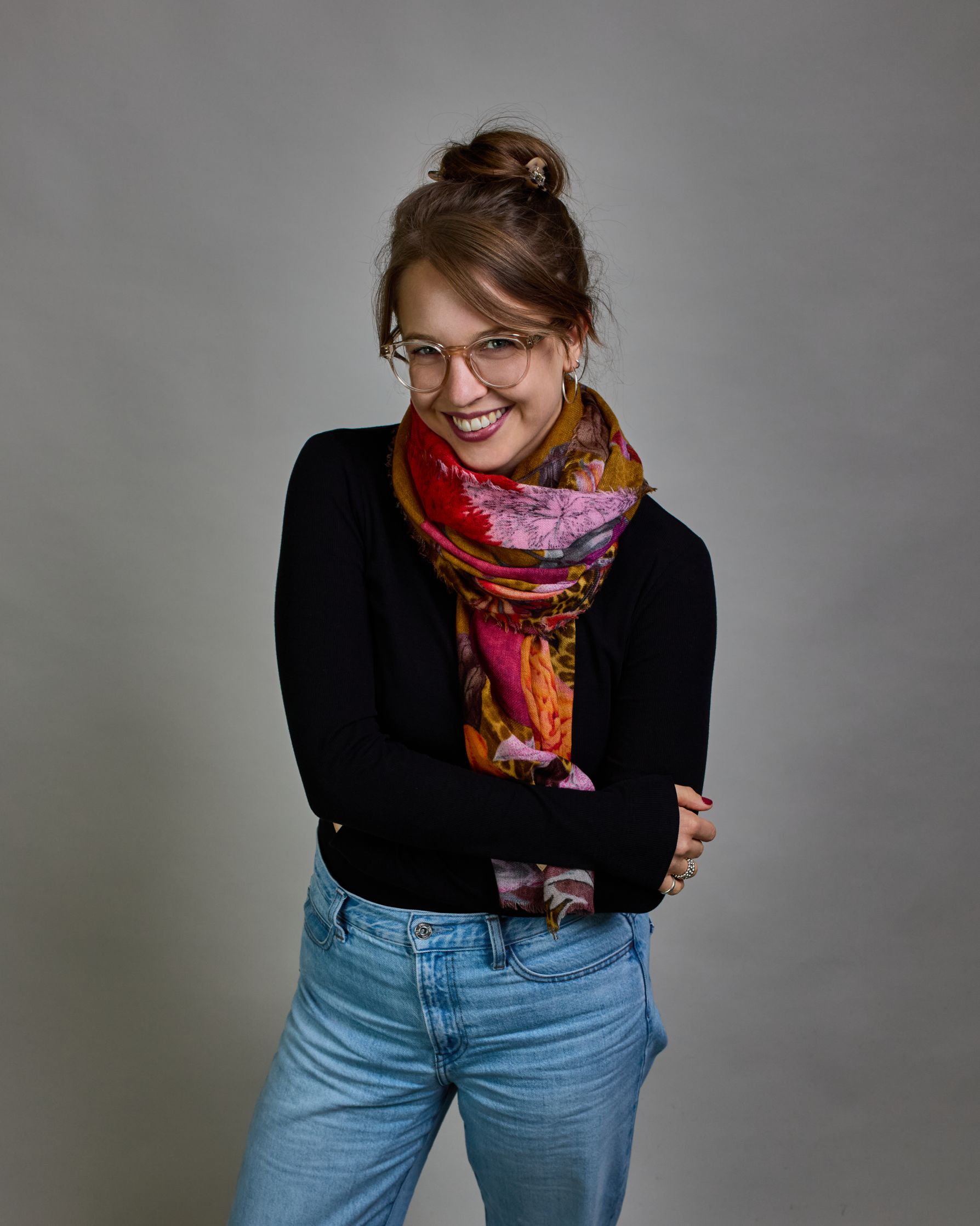 Ein Schal aus 75 % Wolle und 25 % Modal mit den Maßen 70 × 180 cm. Je nach Bild ist er locker um den Nacken gelegt oder einmal gewickelt, um eine lockere Schlaufe um den Hals zu haben, oder zweimal gewickelt, um das Maximum an Wärme zu bekommen. An den Kanten ist er leicht gefranst. Die Hintergrundfarbe des Schals ist Okker und hier und da ist ein Leomuster in Brauntönen zu sehen. Auf dem ganzen Schal sind Blumen in Rot-, Orange-, Weiß- und Pinktönen sowie Blätter beziehungsweise Blumenstängel in verschied…