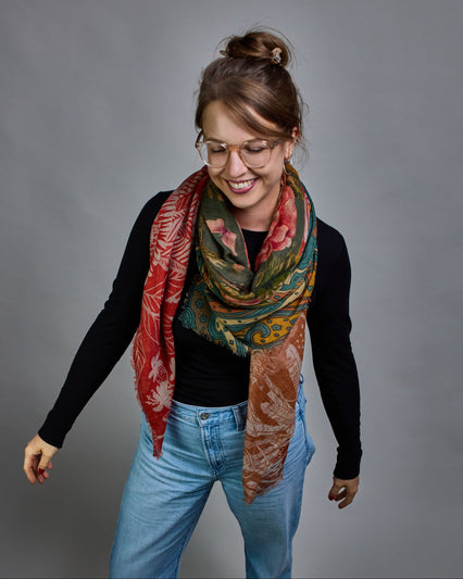 Ein Schal aus 90 % Wolle und 10% Seide. Je nach Bild ist er locker um den Nacken gelegt oder einmal gewickelt, um eine lockere Schlaufe um den Hals zu haben, oder zweimal gewickelt, um das Maximum an Wärme zu bekommen. An den Kanten ist er leicht gefranst. Das Design ist in 4 gleichgroße Quadrate aufgeteilt die jeweils ein anderes Muster hat. Die Quadrate sind mit einem aufgenähtem Okkerfarbenen Samtband unterteilt. Eines der Quadrate hat als Grundfarbe Petrol und darauf befinden sich in verschiedenen Rosa…