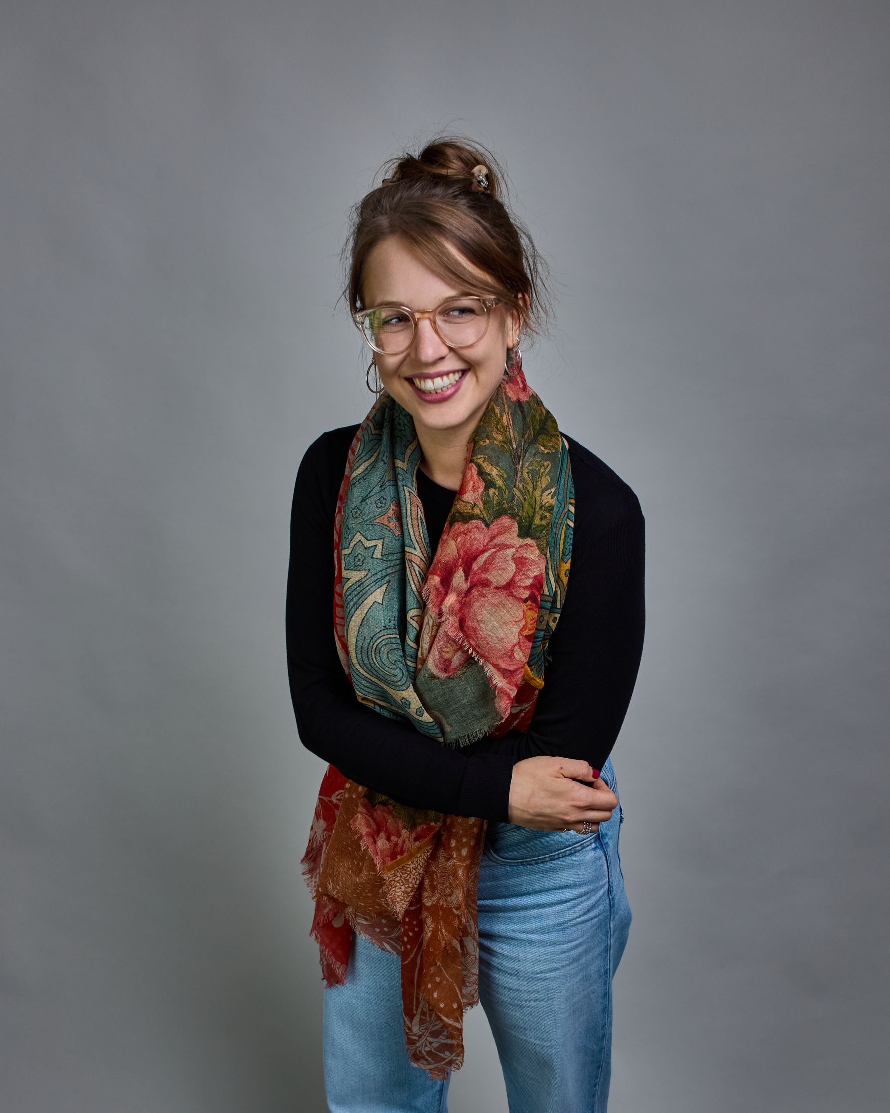 Ein Schal aus 90 % Wolle und 10% Seide. Je nach Bild ist er locker um den Nacken gelegt oder einmal gewickelt, um eine lockere Schlaufe um den Hals zu haben, oder zweimal gewickelt, um das Maximum an Wärme zu bekommen. An den Kanten ist er leicht gefranst. Das Design ist in 4 gleichgroße Quadrate aufgeteilt die jeweils ein anderes Muster hat. Die Quadrate sind mit einem aufgenähtem Okkerfarbenen Samtband unterteilt. Eines der Quadrate hat als Grundfarbe Petrol und darauf befinden sich in verschiedenen Rosa…