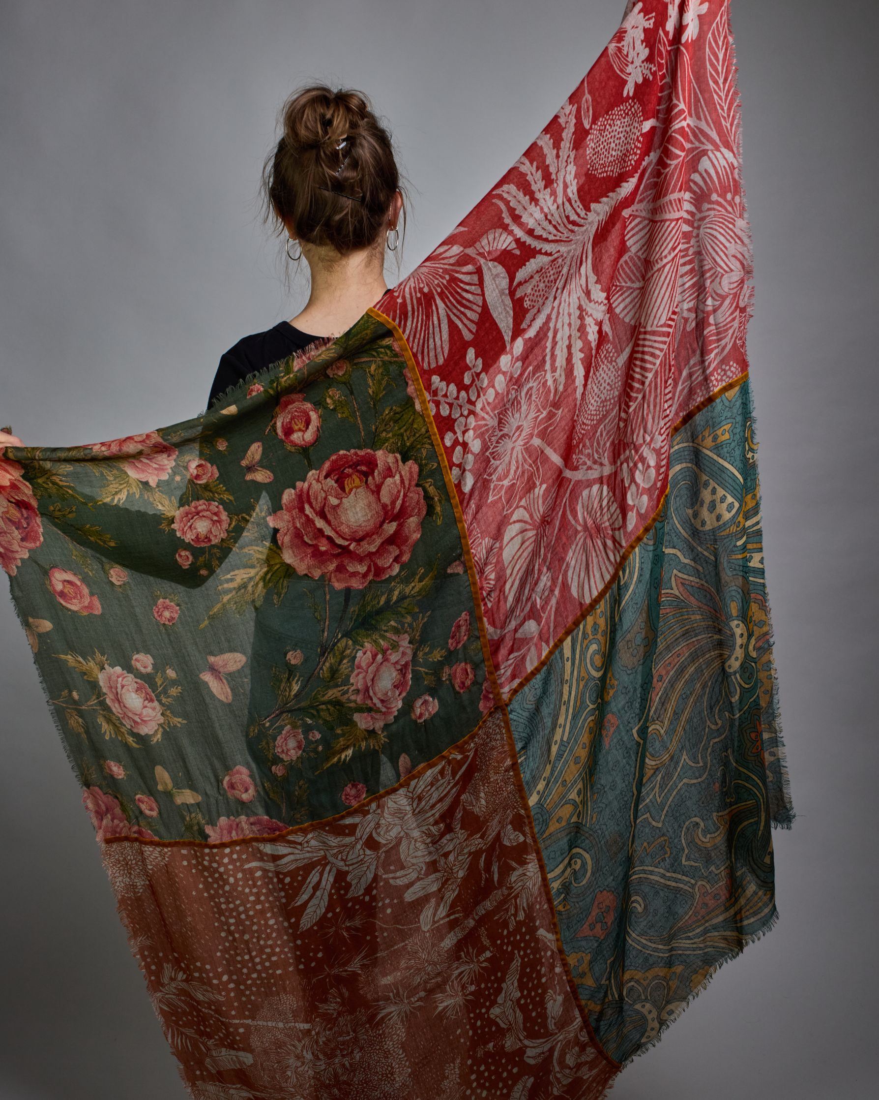 Ein Schal aus 90 % Wolle und 10% Seide. Je nach Bild ist er locker um den Nacken gelegt oder einmal gewickelt, um eine lockere Schlaufe um den Hals zu haben, oder zweimal gewickelt, um das Maximum an Wärme zu bekommen. An den Kanten ist er leicht gefranst. Das Design ist in 4 gleichgroße Quadrate aufgeteilt die jeweils ein anderes Muster hat. Die Quadrate sind mit einem aufgenähtem Okkerfarbenen Samtband unterteilt. Eines der Quadrate hat als Grundfarbe Petrol und darauf befinden sich in verschiedenen Rosa…