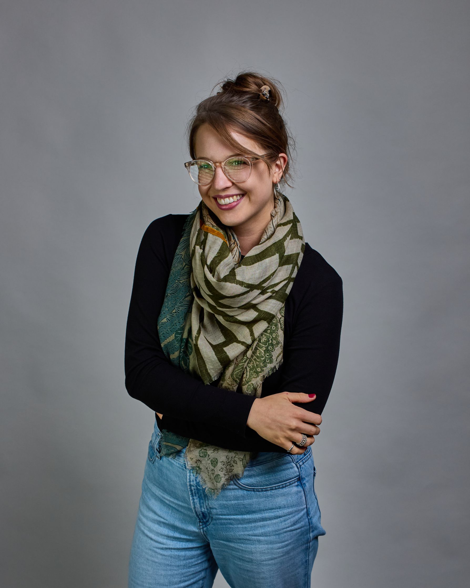 Ein Schal aus 90 % Wolle und 10% Seide. Je nach Bild ist er locker um den Nacken gelegt oder einmal gewickelt, um eine lockere Schlaufe um den Hals zu haben, oder zweimal gewickelt, um das Maximum an Wärme zu bekommen. An den Kanten ist er leicht gefranst. Das Design ist in 4 gleichgroße Quadrate aufgeteilt die jeweils ein anderes Muster hat. Die Quadrate sind mit einem aufgenähtem Okkerfarbenen Samtband unterteilt. Eines der Quadrate hat als Grundfarbe Cremeweiß und darauf befinden sich in verschiedenen G…