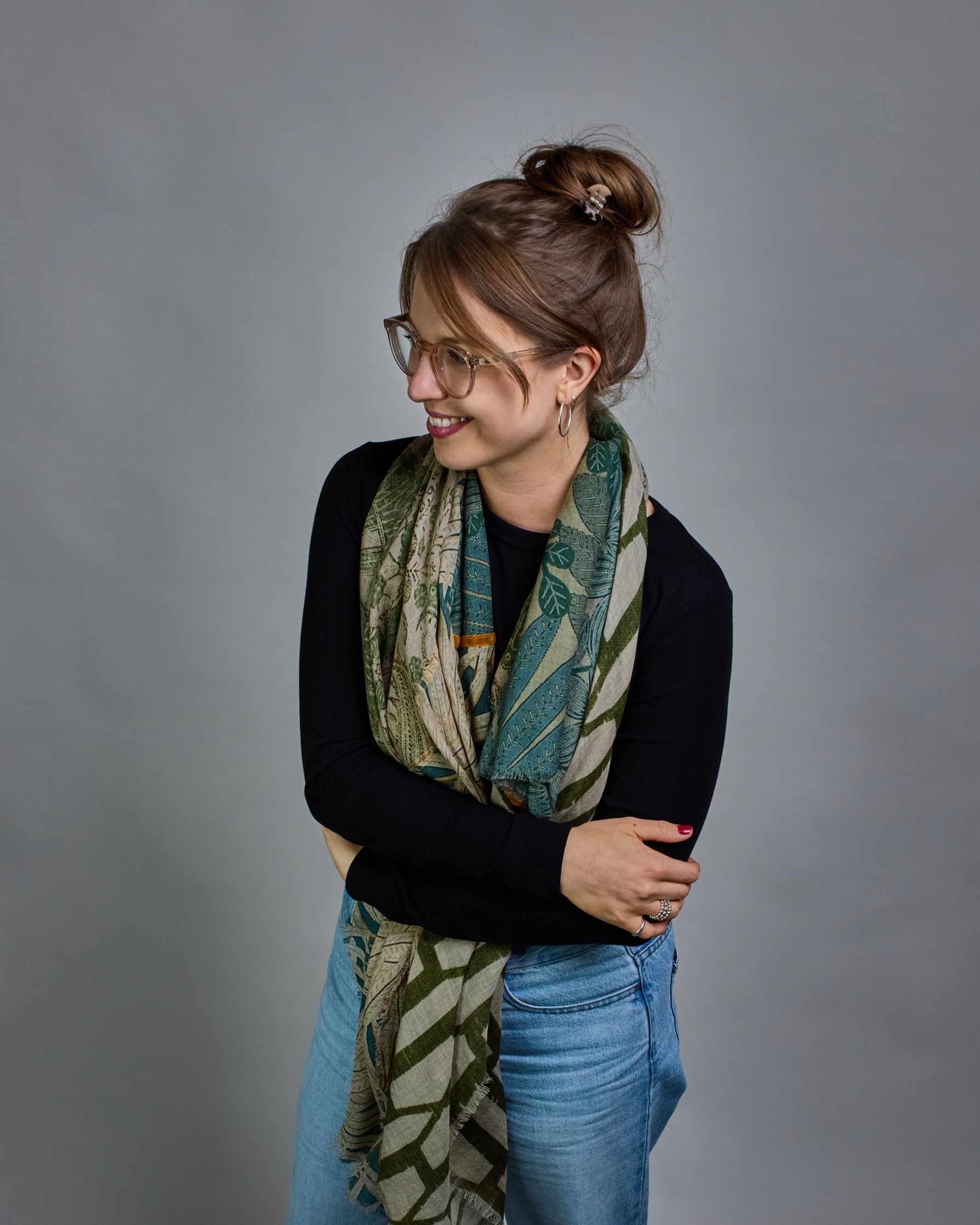 Ein Schal aus 90 % Wolle und 10% Seide. Je nach Bild ist er locker um den Nacken gelegt oder einmal gewickelt, um eine lockere Schlaufe um den Hals zu haben, oder zweimal gewickelt, um das Maximum an Wärme zu bekommen. An den Kanten ist er leicht gefranst. Das Design ist in 4 gleichgroße Quadrate aufgeteilt die jeweils ein anderes Muster hat. Die Quadrate sind mit einem aufgenähtem Okkerfarbenen Samtband unterteilt. Eines der Quadrate hat als Grundfarbe Cremeweiß und darauf befinden sich in verschiedenen G…