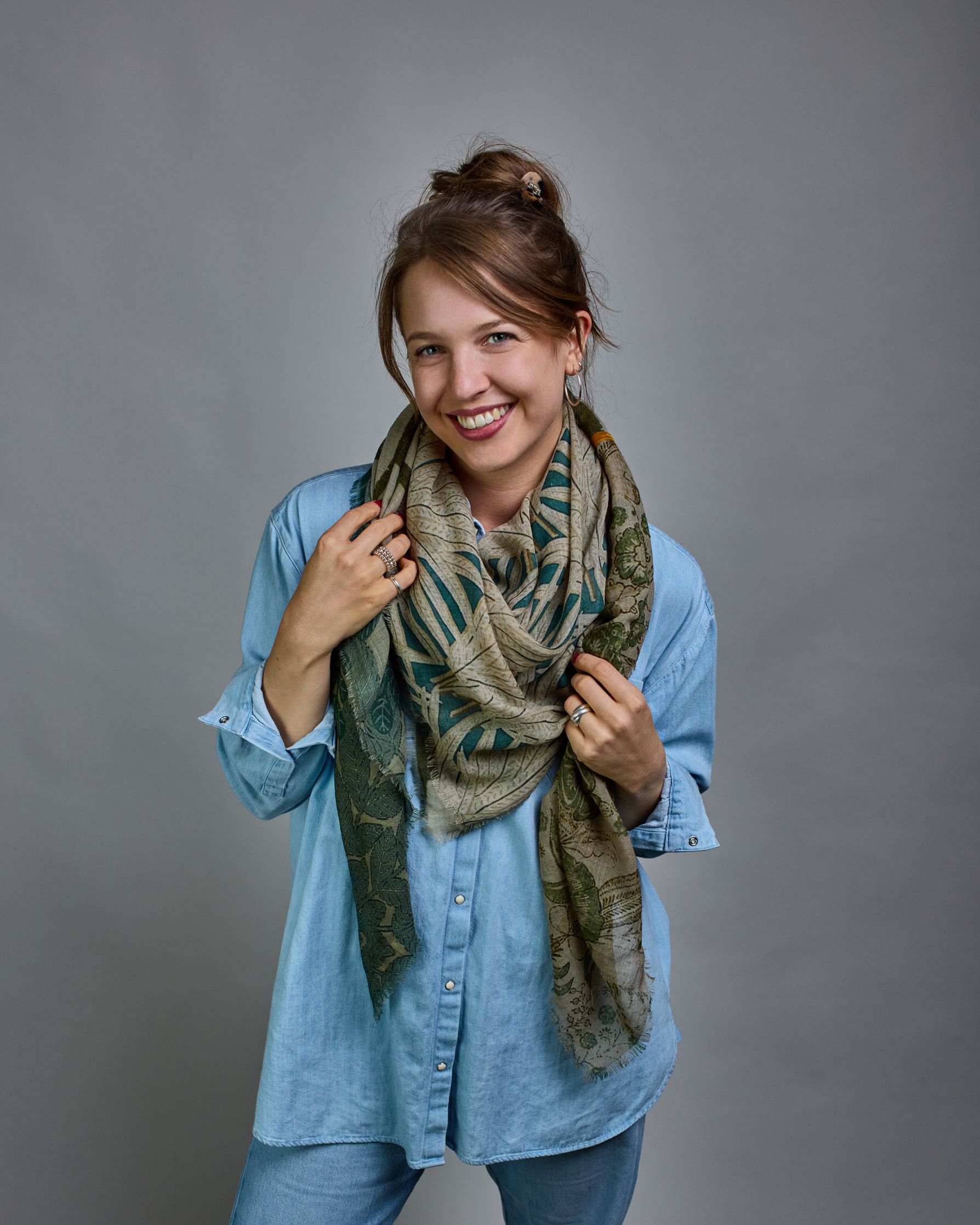 Ein Schal aus 90 % Wolle und 10% Seide. Je nach Bild ist er locker um den Nacken gelegt oder einmal gewickelt, um eine lockere Schlaufe um den Hals zu haben, oder zweimal gewickelt, um das Maximum an Wärme zu bekommen. An den Kanten ist er leicht gefranst. Das Design ist in 4 gleichgroße Quadrate aufgeteilt die jeweils ein anderes Muster hat. Die Quadrate sind mit einem aufgenähtem Okkerfarbenen Samtband unterteilt. Eines der Quadrate hat als Grundfarbe Cremeweiß und darauf befinden sich in verschiedenen G…