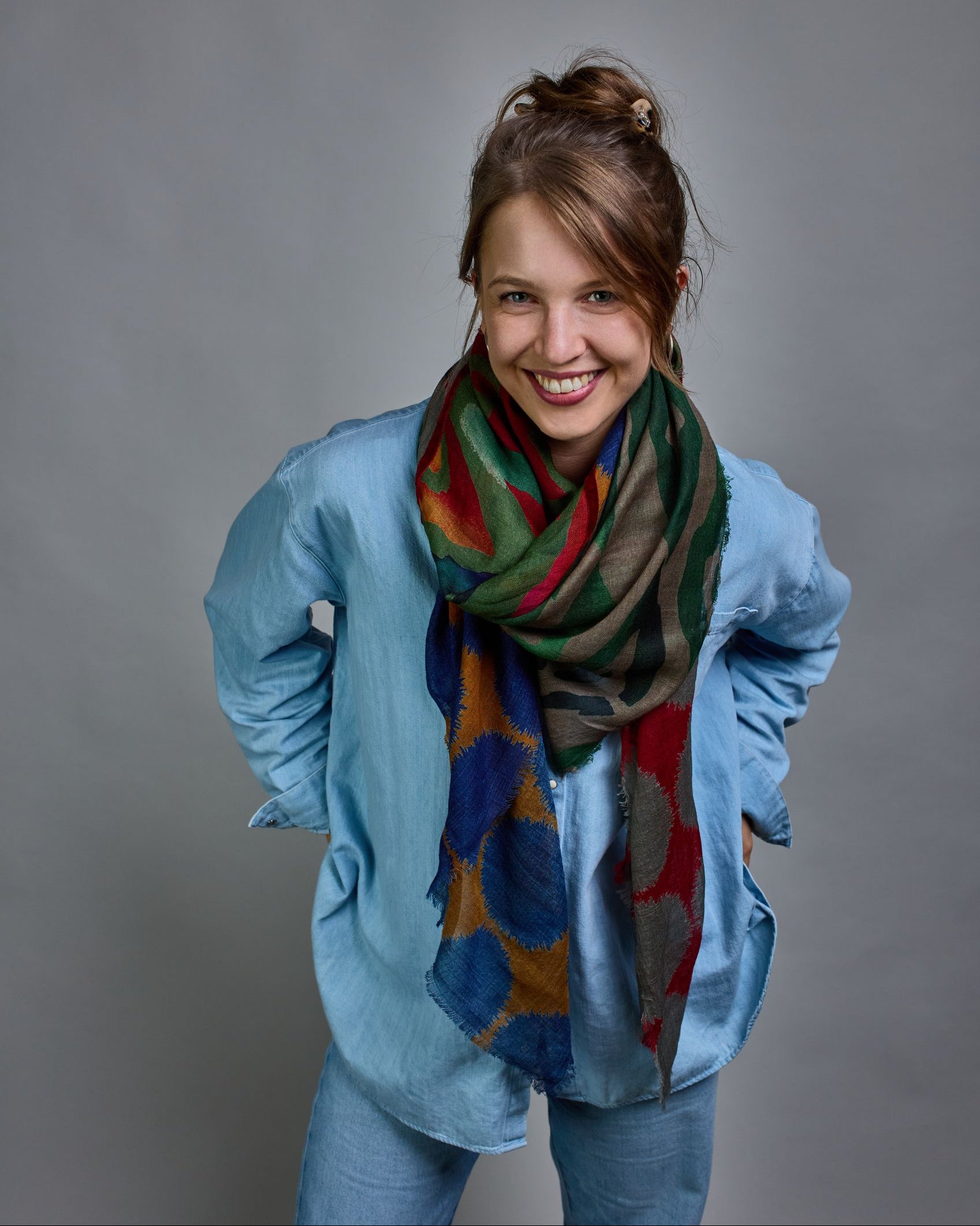 Ein Schal aus 90 % Wolle und 10% Seide. Je nach Bild ist er locker um den Nacken gelegt oder einmal gewickelt, um eine lockere Schlaufe um den Hals zu haben, oder zweimal gewickelt, um das Maximum an Wärme zu bekommen. An den Kanten ist er leicht gefranst. Das Design ist in 4 gleichgroße Quadrate aufgeteilt die jeweils ein anderes Muster hat. Die Quadrate sind mit einem aufgenähtem Rotem Samtband unterteilt. Eines der Quadrate hat als Grundfarbe Okker und darauf befinden sich fransige Kreise in Blau. Im nä…