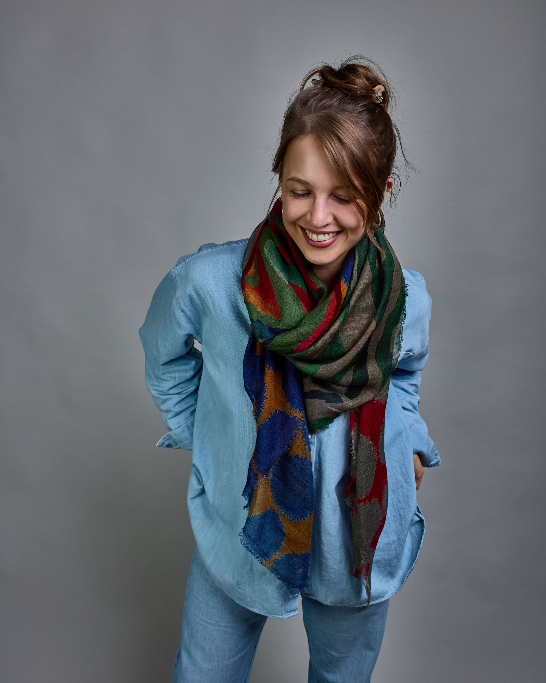 Ein Schal aus 90 % Wolle und 10% Seide. Je nach Bild ist er locker um den Nacken gelegt oder einmal gewickelt, um eine lockere Schlaufe um den Hals zu haben, oder zweimal gewickelt, um das Maximum an Wärme zu bekommen. An den Kanten ist er leicht gefranst. Das Design ist in 4 gleichgroße Quadrate aufgeteilt die jeweils ein anderes Muster hat. Die Quadrate sind mit einem aufgenähtem Rotem Samtband unterteilt. Eines der Quadrate hat als Grundfarbe Okker und darauf befinden sich fransige Kreise in Blau. Im nä…