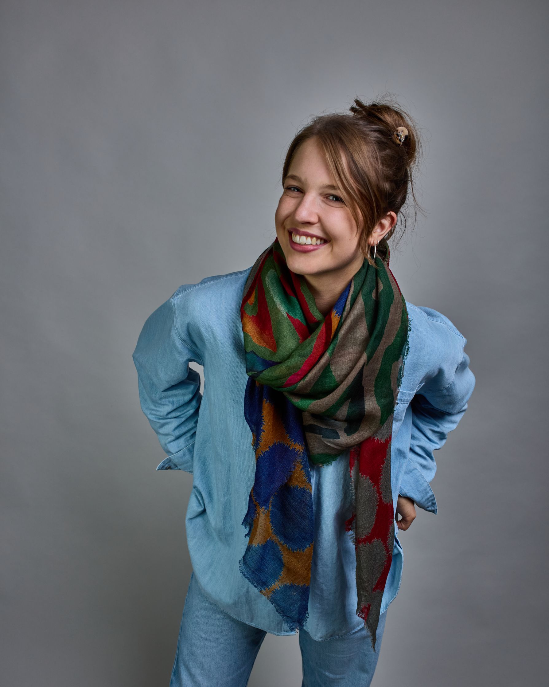 Ein Schal aus 90 % Wolle und 10% Seide. Je nach Bild ist er locker um den Nacken gelegt oder einmal gewickelt, um eine lockere Schlaufe um den Hals zu haben, oder zweimal gewickelt, um das Maximum an Wärme zu bekommen. An den Kanten ist er leicht gefranst. Das Design ist in 4 gleichgroße Quadrate aufgeteilt die jeweils ein anderes Muster hat. Die Quadrate sind mit einem aufgenähtem Rotem Samtband unterteilt. Eines der Quadrate hat als Grundfarbe Okker und darauf befinden sich fransige Kreise in Blau. Im nä…