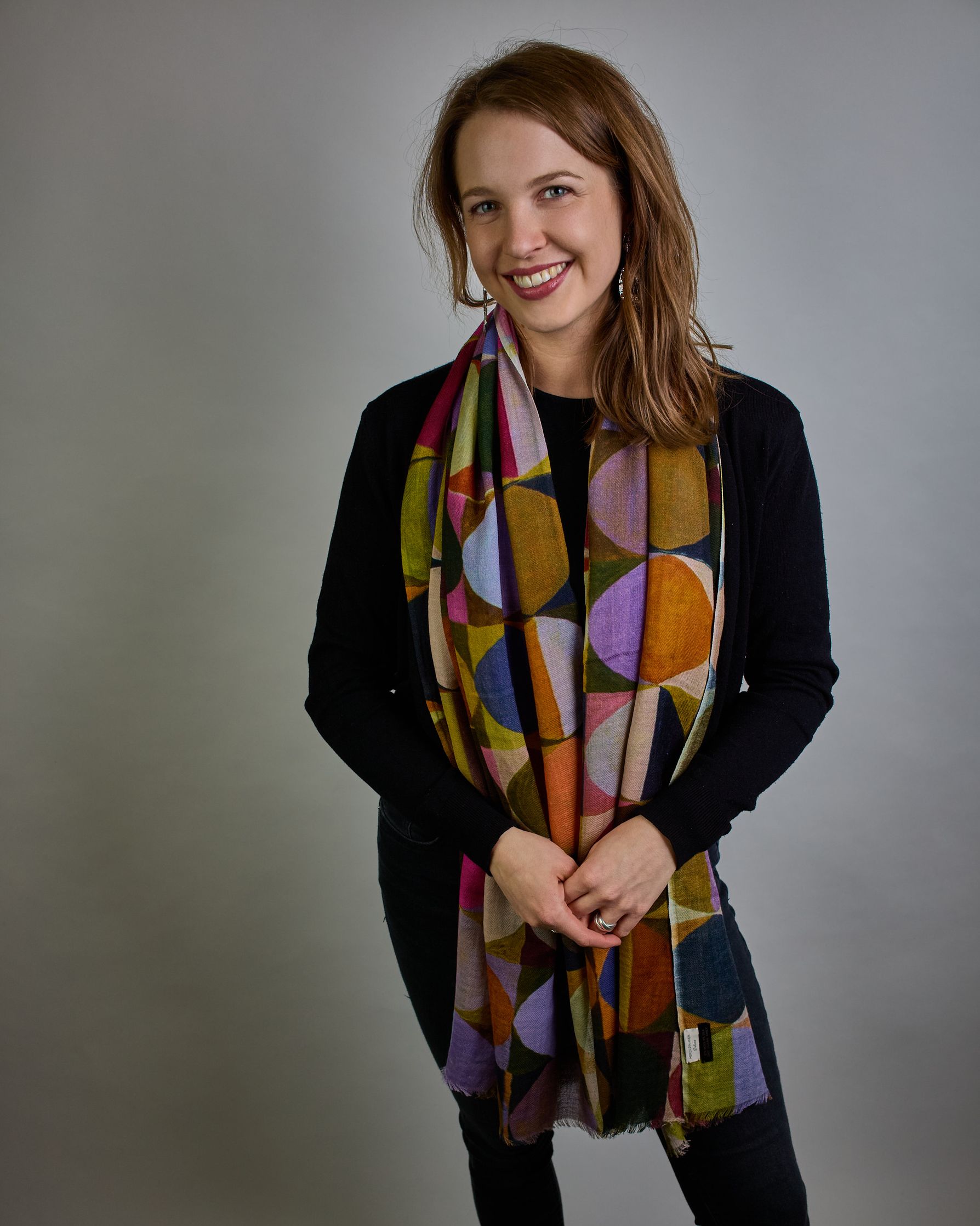 Ein Schal aus 75 % Wolle und 25 % Modal mit den Maßen 100 × 180 cm. Je nach Bild ist er locker um den Nacken gelegt oder einmal gewickelt, um eine lockere Schlaufe um den Hals zu haben, oder zweimal gewickelt, um das Maximum an Wärme zu bekommen. An den Kanten ist er leicht gefranst. Über den ganzen Schal ist ein symetrisches Kreismuster verteilt. Die Dreiecke sind in Grau-, Rot-, Blau- Rosa-, Lila-, Grün- und Brauntönen gehalten. #3