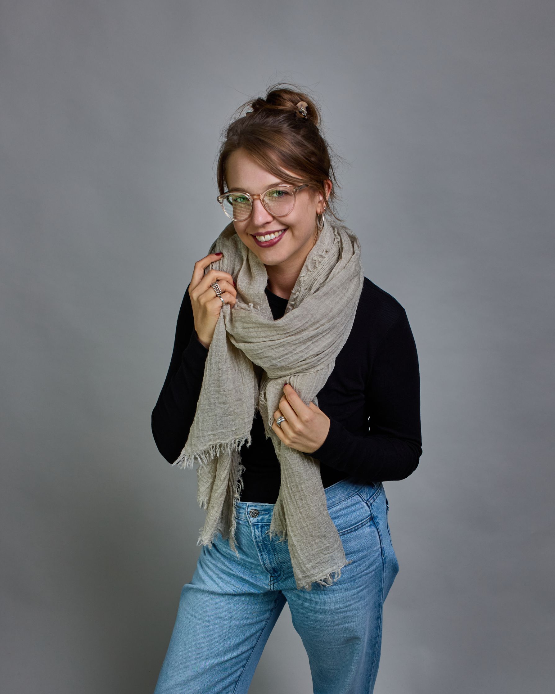 Ein beiger Schal aus 100 % Wolle mit den Maßen 100x180 cm. Je nach Bild ist er locker um den Hals gelegt oder einmal gewickelt, um eine Schlaufe um den Hals zu haben. Der Schal ist einfärbig und hat an den Kanten leichte Fransen. Die organische Struktur verleiht dem Schal ein lässiges, zeitloses Design. #2