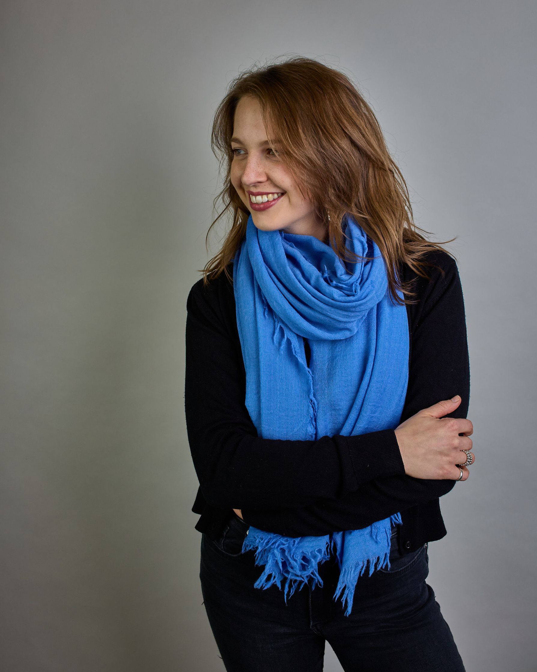 Ein Schal aus 100 % Wolle in einem kaltem Mittel Blauton mit den Maßen 100x180 cm. Je nach Bild ist er locker um den Hals gelegt oder einmal gewickelt, um eine Schlaufe um den Hals zu haben. Der Schal ist einfärbig und hat an den Kanten leichte Fransen. Die organische Struktur verleiht dem Schal ein lässiges, zeitloses Design. #4