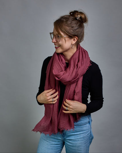 Ein bordeauxfarbener Schal aus 100 % Wolle mit den Maßen 100x180 cm. Je nach Bild ist er locker um den Hals gelegt oder einmal gewickelt, um eine Schlaufe um den Hals zu haben. Der Schal ist einfärbig und hat an den Kanten leichte Fransen. Die organische Struktur verleiht dem Schal ein lässiges, zeitloses Design. #2