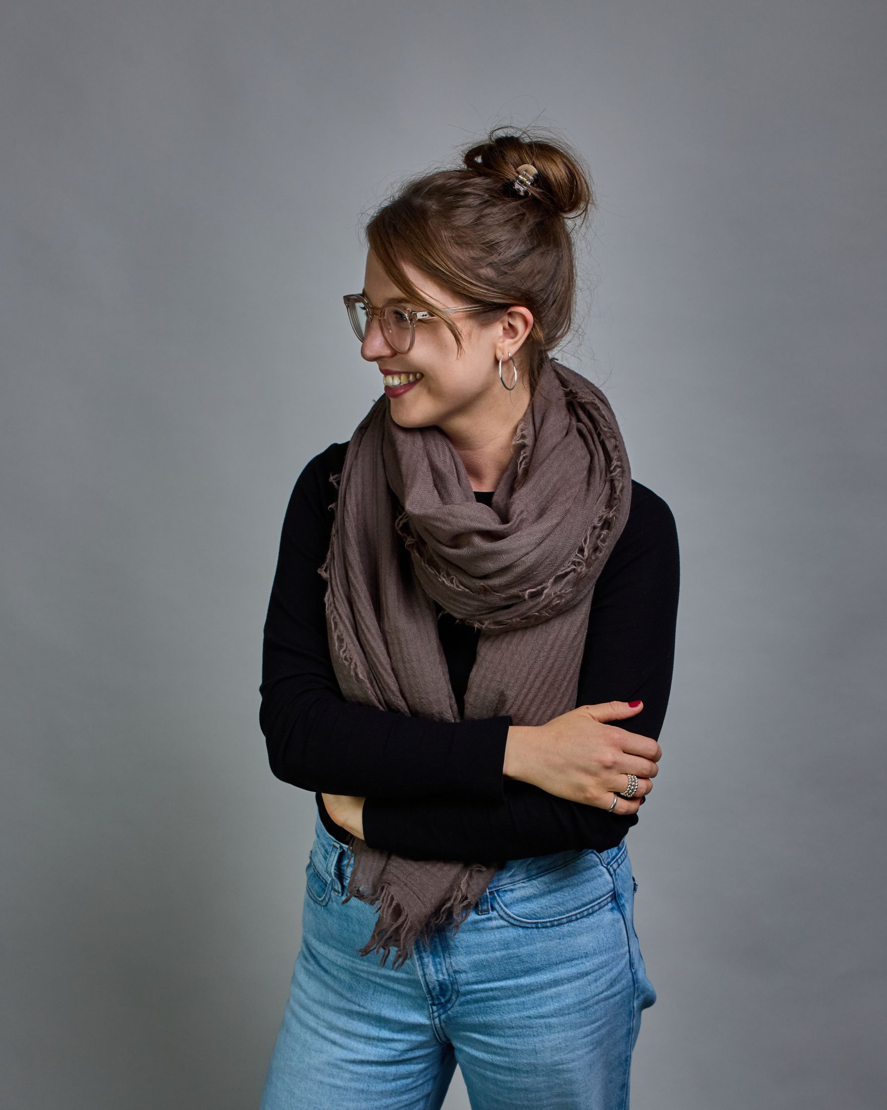 Ein Schal aus 100 % Wolle in einem kaltem Braunton mit den Maßen 100x180 cm. Je nach Bild ist er locker um den Hals gelegt oder einmal gewickelt, um eine Schlaufe um den Hals zu haben. Der Schal ist einfärbig und hat an den Kanten leichte Fransen. Die organische Struktur verleiht dem Schal ein lässiges, zeitloses Design. #2