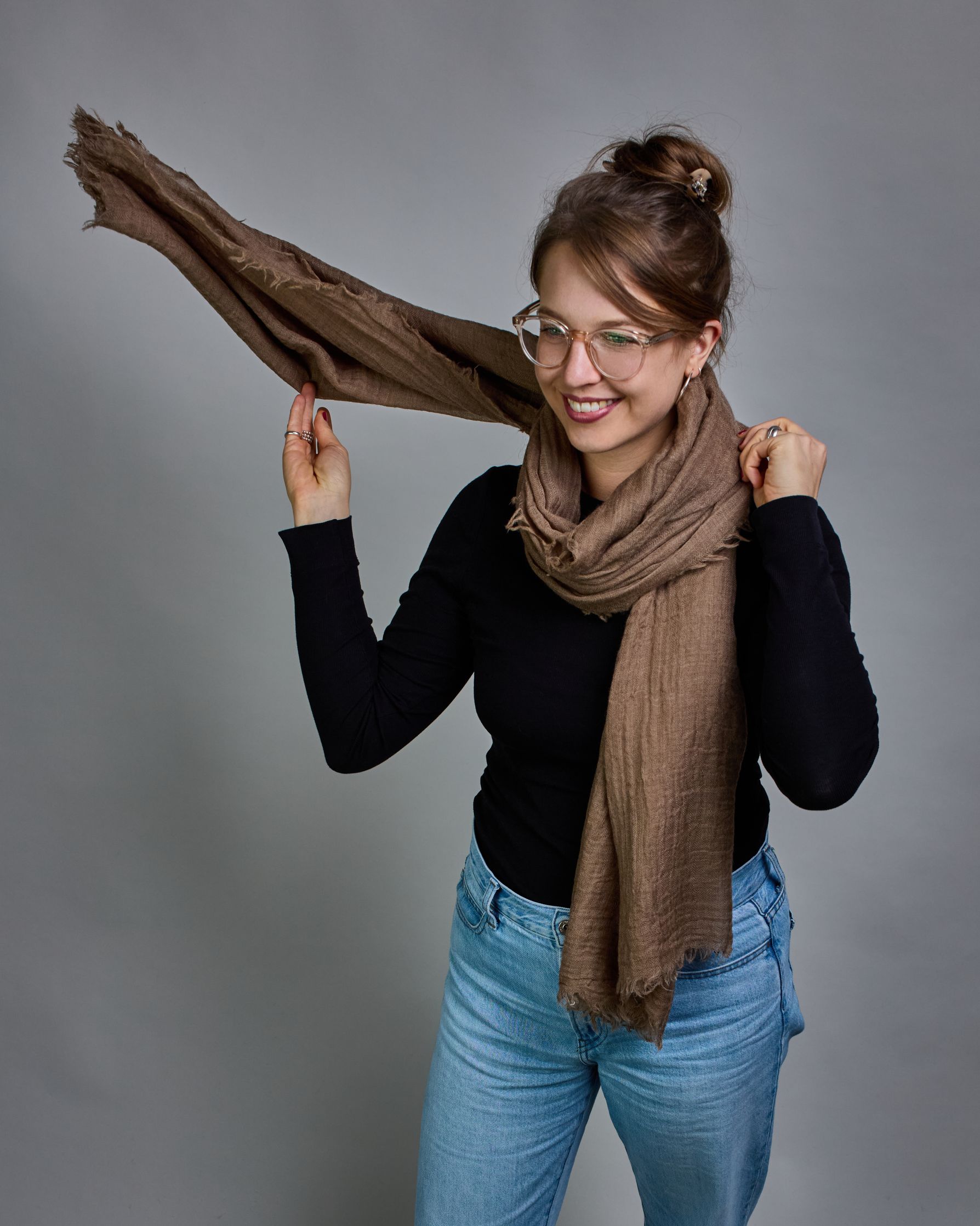 Ein cognacfarbener Schal aus 100 % Wolle mit den Maßen 100x180 cm. Je nach Bild ist er locker um den Hals gelegt oder einmal gewickelt, um eine Schlaufe um den Hals zu haben. Der Schal ist einfärbig und hat an den Kanten leichte Fransen. Die organische Struktur verleiht dem Schal ein lässiges, zeitloses Design. #2