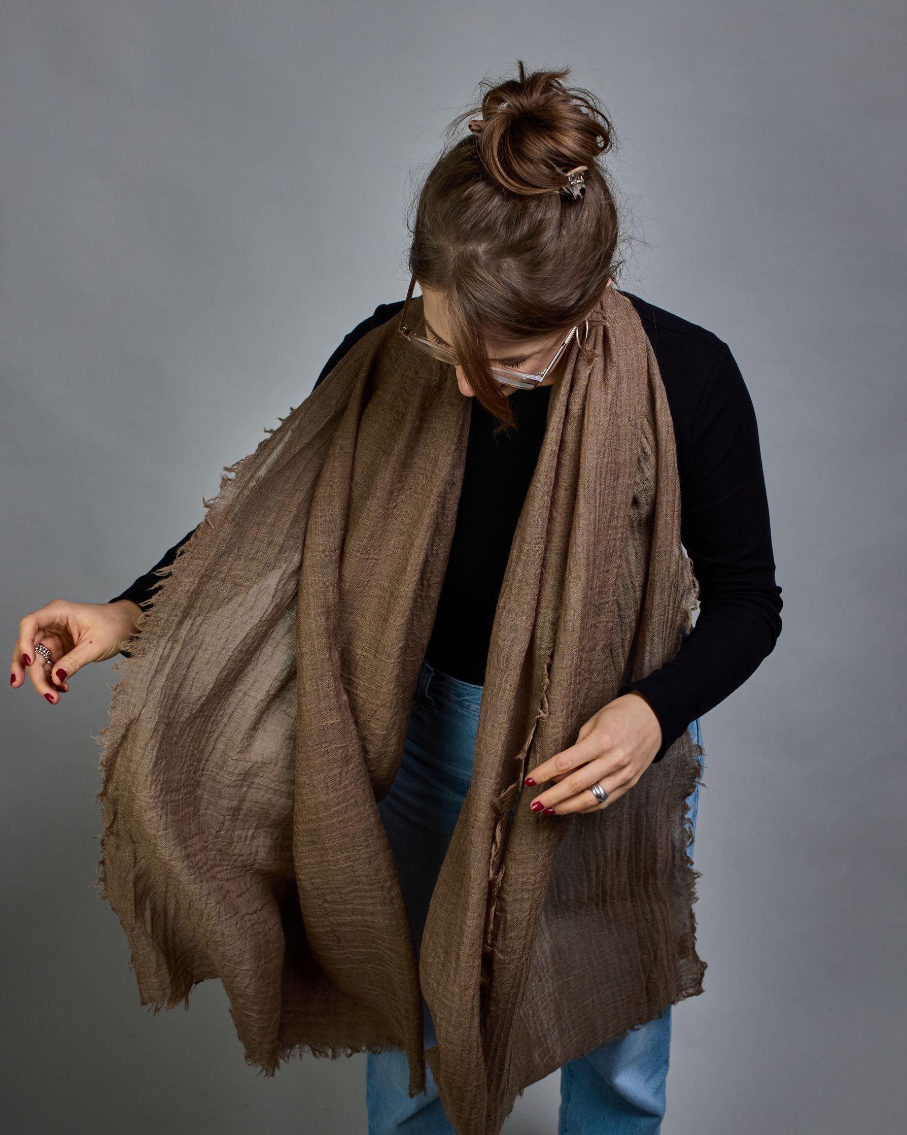 Ein cognacfarbener Schal aus 100 % Wolle mit den Maßen 100x180 cm. Je nach Bild ist er locker um den Hals gelegt oder einmal gewickelt, um eine Schlaufe um den Hals zu haben. Der Schal ist einfärbig und hat an den Kanten leichte Fransen. Die organische Struktur verleiht dem Schal ein lässiges, zeitloses Design. #3