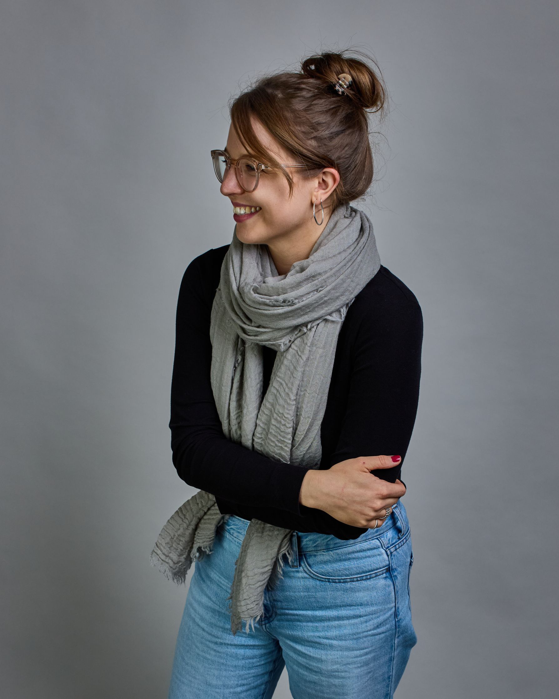 Ein hellgrauer Schal aus 100 % Wolle mit den Maßen 100x180 cm. Je nach Bild ist er locker um den Hals gelegt oder einmal gewickelt, um eine Schlaufe um den Hals zu haben. Der Schal ist einfärbig und hat an den Kanten leichte Fransen. Die organische Struktur verleiht dem Schal ein lässiges, zeitloses Design. #1