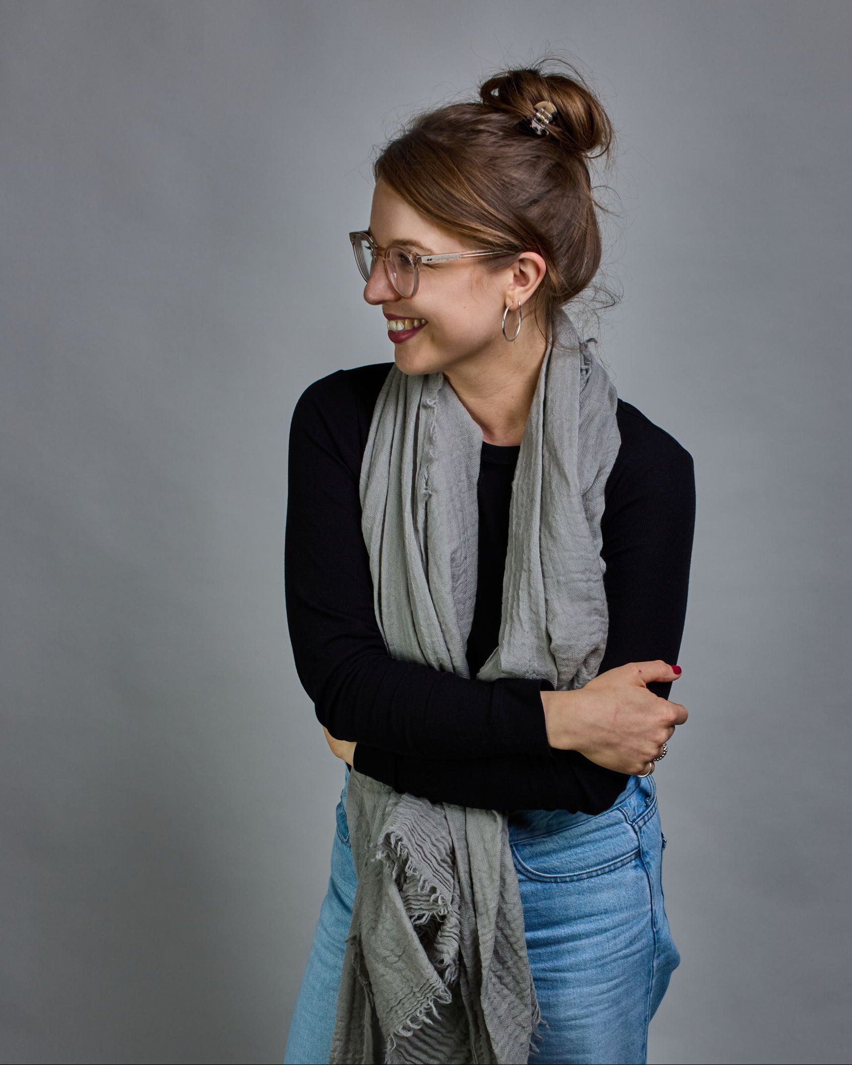 Ein hellgrauer Schal aus 100 % Wolle mit den Maßen 100x180 cm. Je nach Bild ist er locker um den Hals gelegt oder einmal gewickelt, um eine Schlaufe um den Hals zu haben. Der Schal ist einfärbig und hat an den Kanten leichte Fransen. Die organische Struktur verleiht dem Schal ein lässiges, zeitloses Design. #3