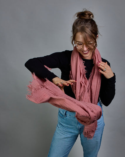 Ein lachsfarbener Schal aus 100 % Wolle mit den Maßen 100x180 cm. Je nach Bild ist er locker um den Hals gelegt oder einmal gewickelt, um eine Schlaufe um den Hals zu haben. Der Schal ist einfärbig und hat an den Kanten leichte Fransen. Die organische Struktur verleiht dem Schal ein lässiges, zeitloses Design. #5