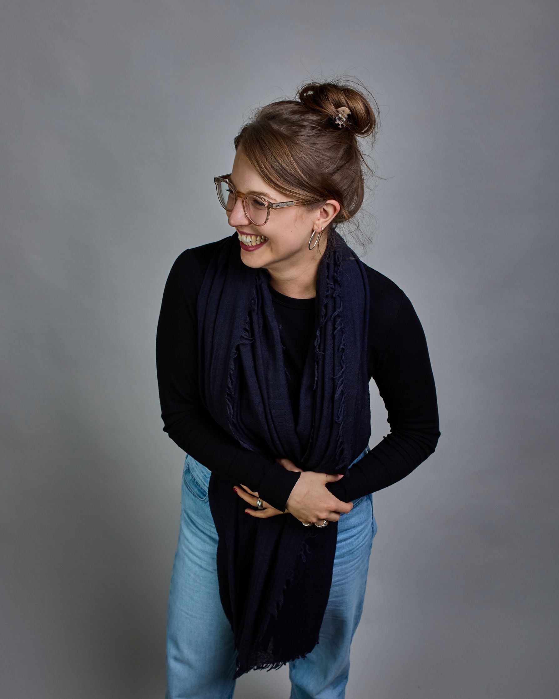 Ein dunkelblauer Schal aus 100 % Wolle mit den Maßen 100x180 cm. Je nach Bild ist er locker um den Hals gelegt oder einmal gewickelt, um eine Schlaufe um den Hals zu haben. Der Schal ist einfärbig und hat an den Kanten leichte Fransen. Die organische Struktur verleiht dem Schal ein lässiges, zeitloses Design. #3