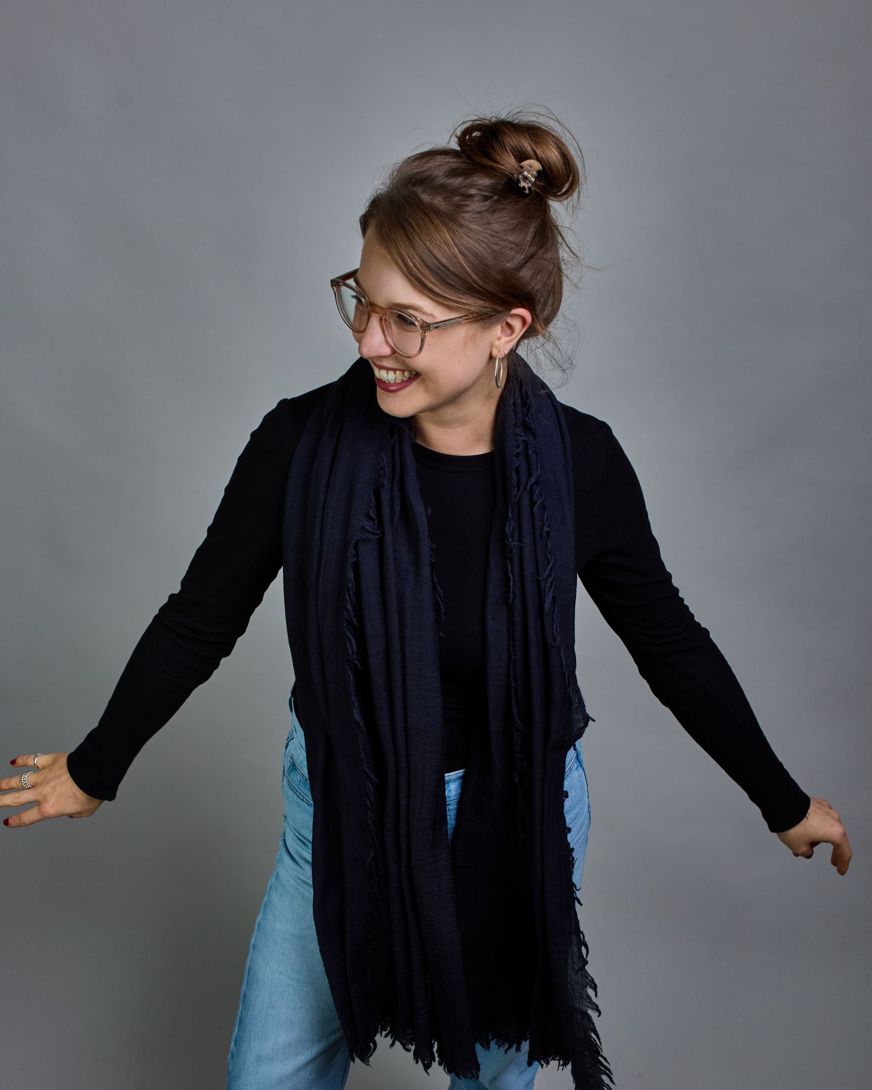 Ein dunkelblauer Schal aus 100 % Wolle mit den Maßen 100x180 cm. Je nach Bild ist er locker um den Hals gelegt oder einmal gewickelt, um eine Schlaufe um den Hals zu haben. Der Schal ist einfärbig und hat an den Kanten leichte Fransen. Die organische Struktur verleiht dem Schal ein lässiges, zeitloses Design. #4