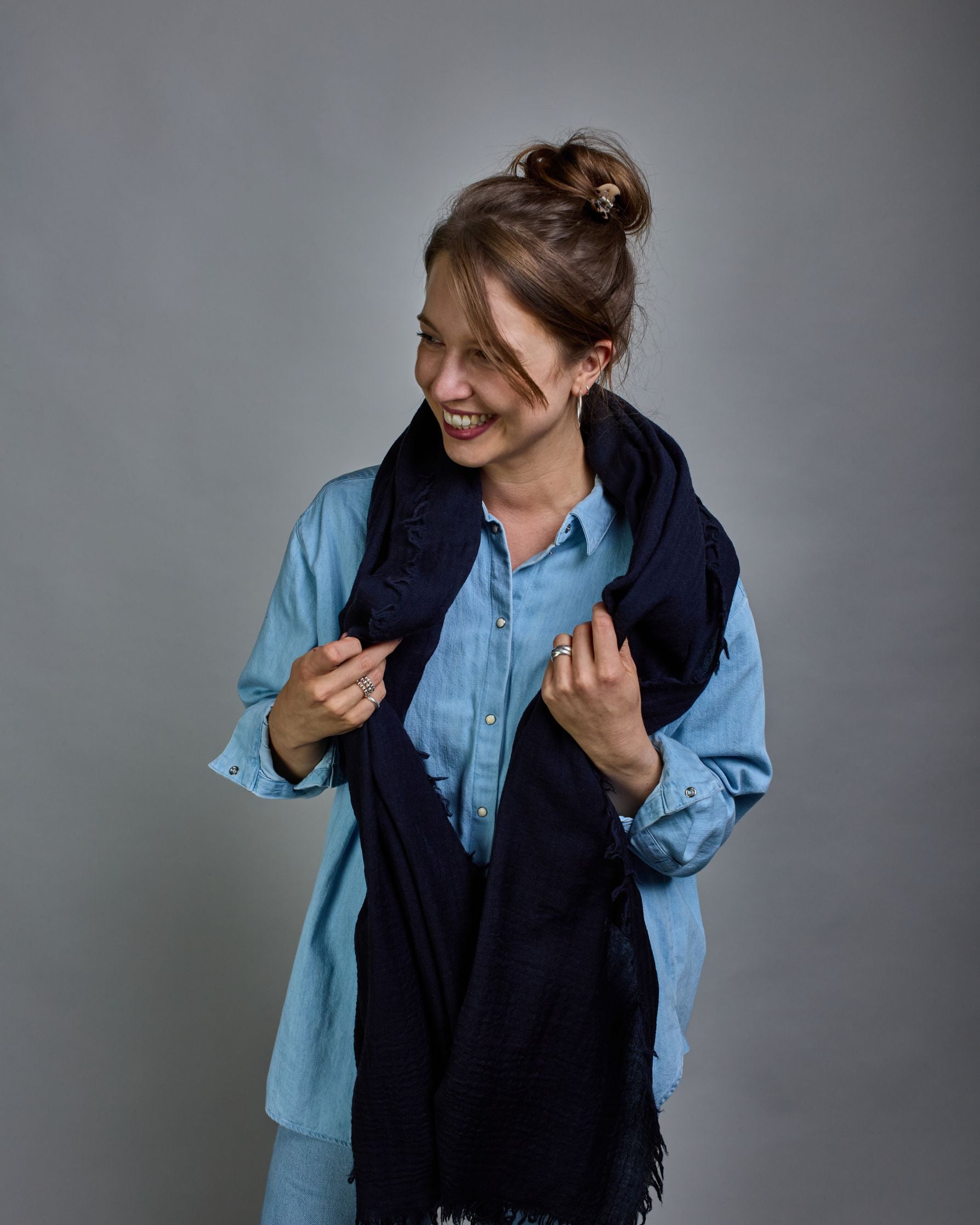 Ein dunkelblauer Schal aus 100 % Wolle mit den Maßen 100x180 cm. Je nach Bild ist er locker um den Hals gelegt oder einmal gewickelt, um eine Schlaufe um den Hals zu haben. Der Schal ist einfärbig und hat an den Kanten leichte Fransen. Die organische Struktur verleiht dem Schal ein lässiges, zeitloses Design. #5