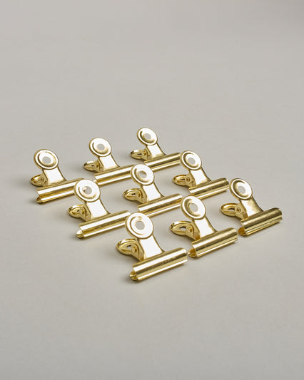 Ein einzelner Metall-Clip in gold mit einem Loch in den Greifarmen an denen man sie oben öffnen kann. #5