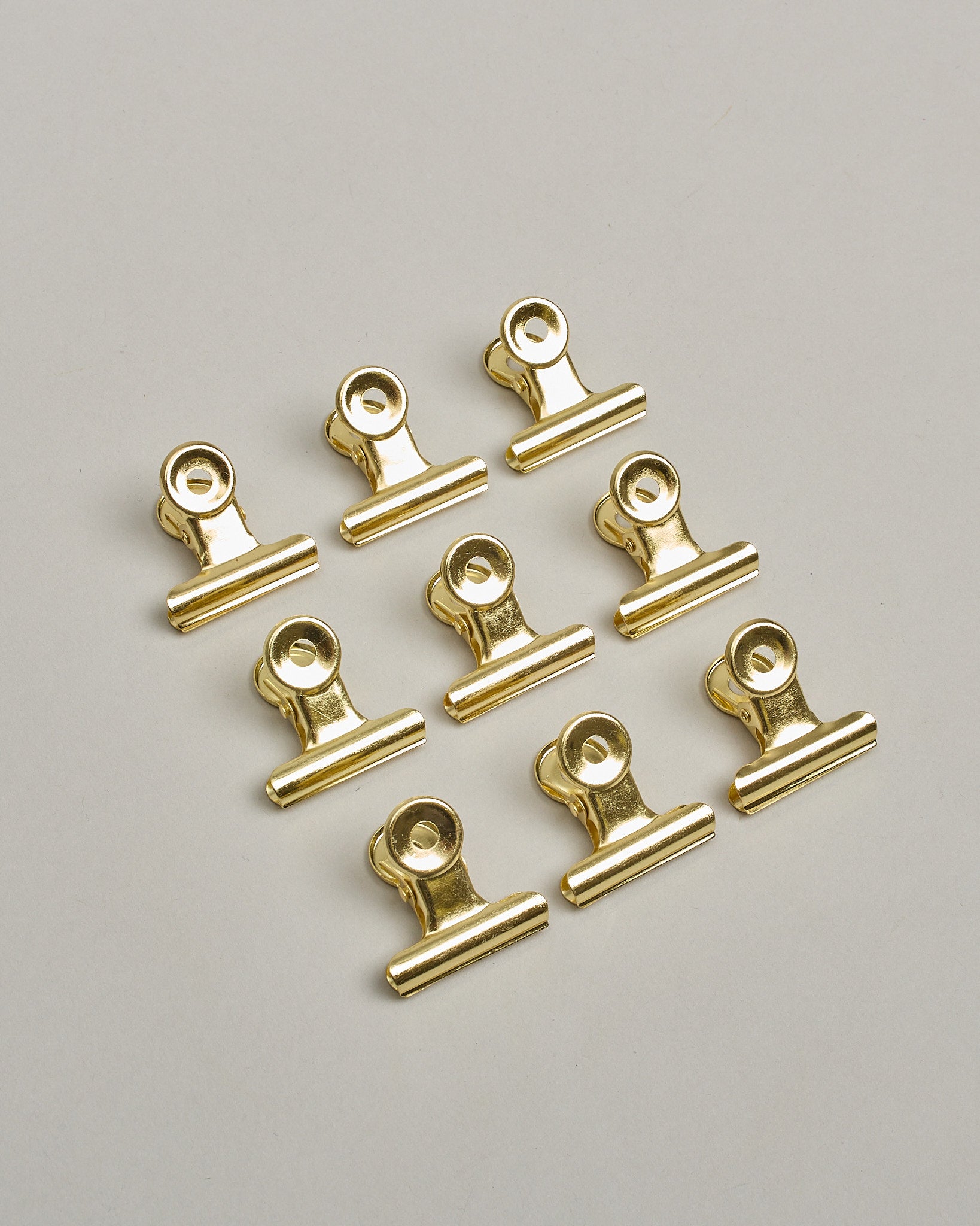 Ein einzelner Metall-Clip in gold mit einem Loch in den Greifarmen an denen man sie oben öffnen kann. #6