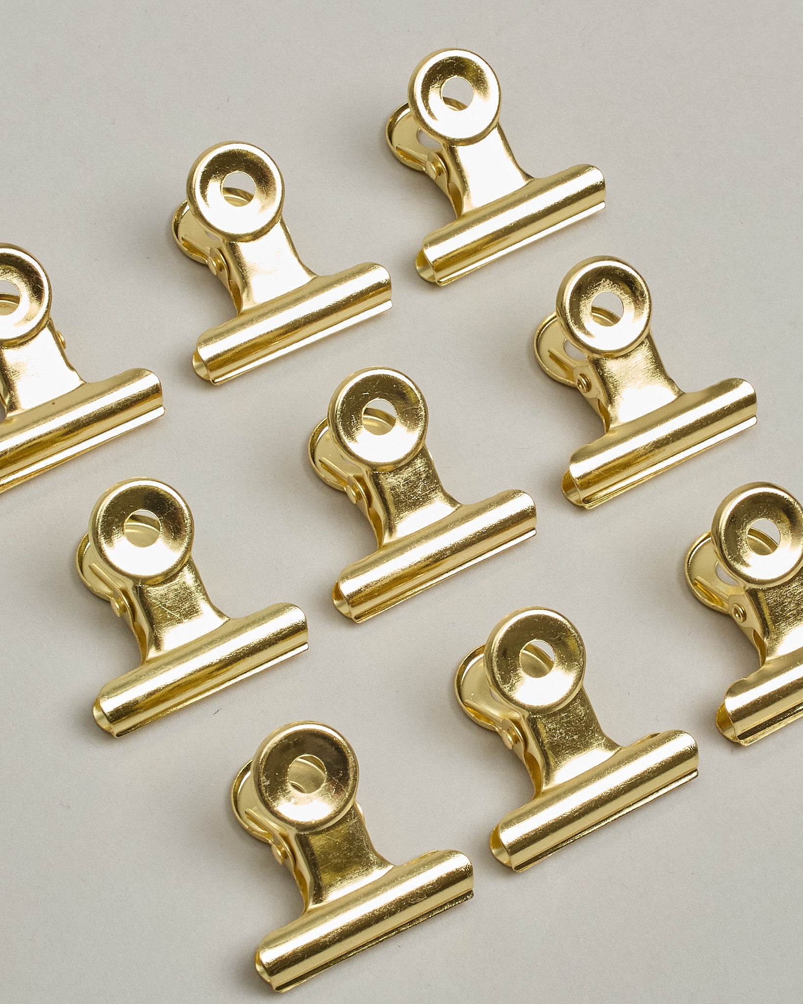 Ein einzelner Metall-Clip in gold mit einem Loch in den Greifarmen an denen man sie oben öffnen kann. #7