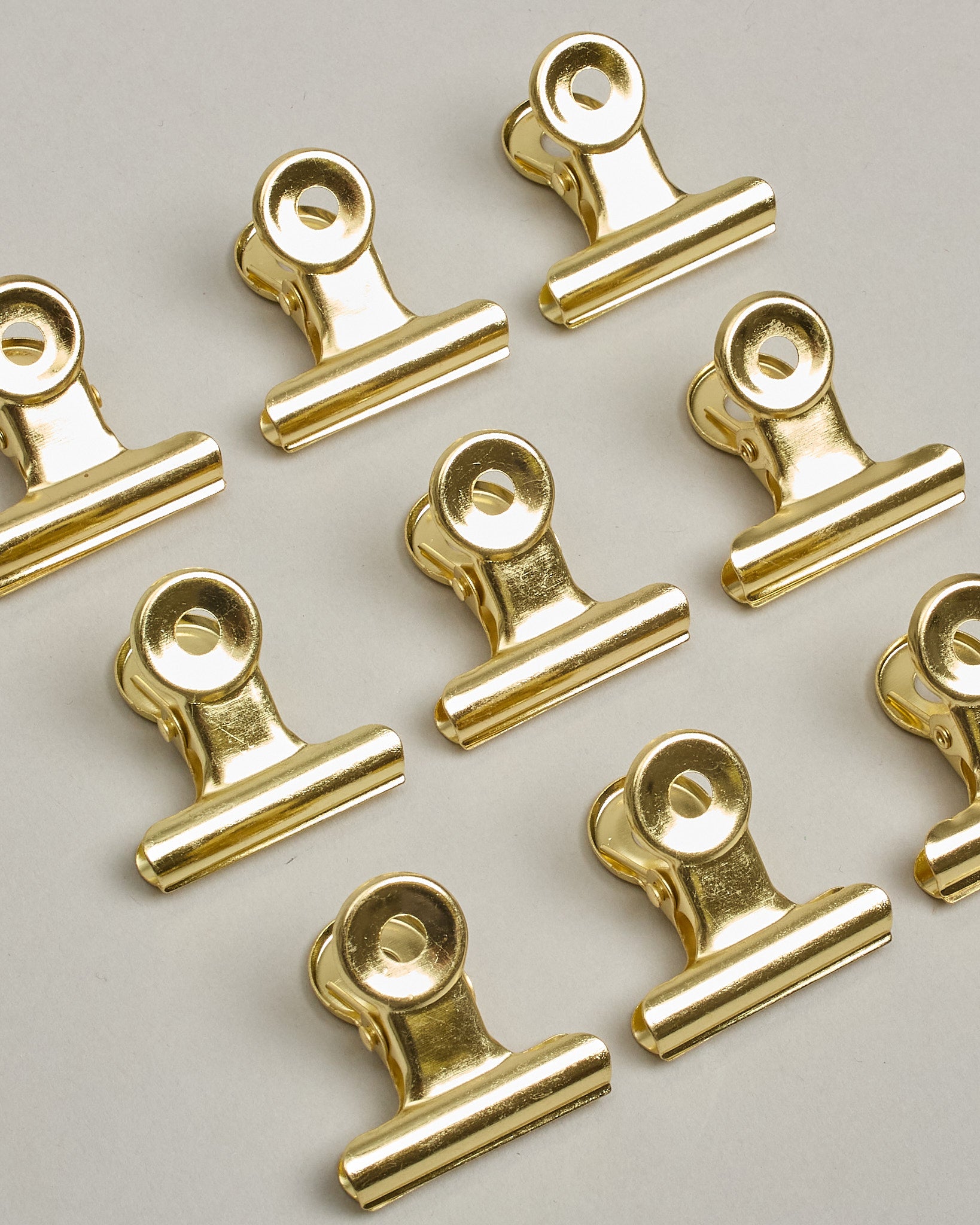 Ein einzelner Metall-Clip in gold mit einem Loch in den Greifarmen an denen man sie oben öffnen kann. #8